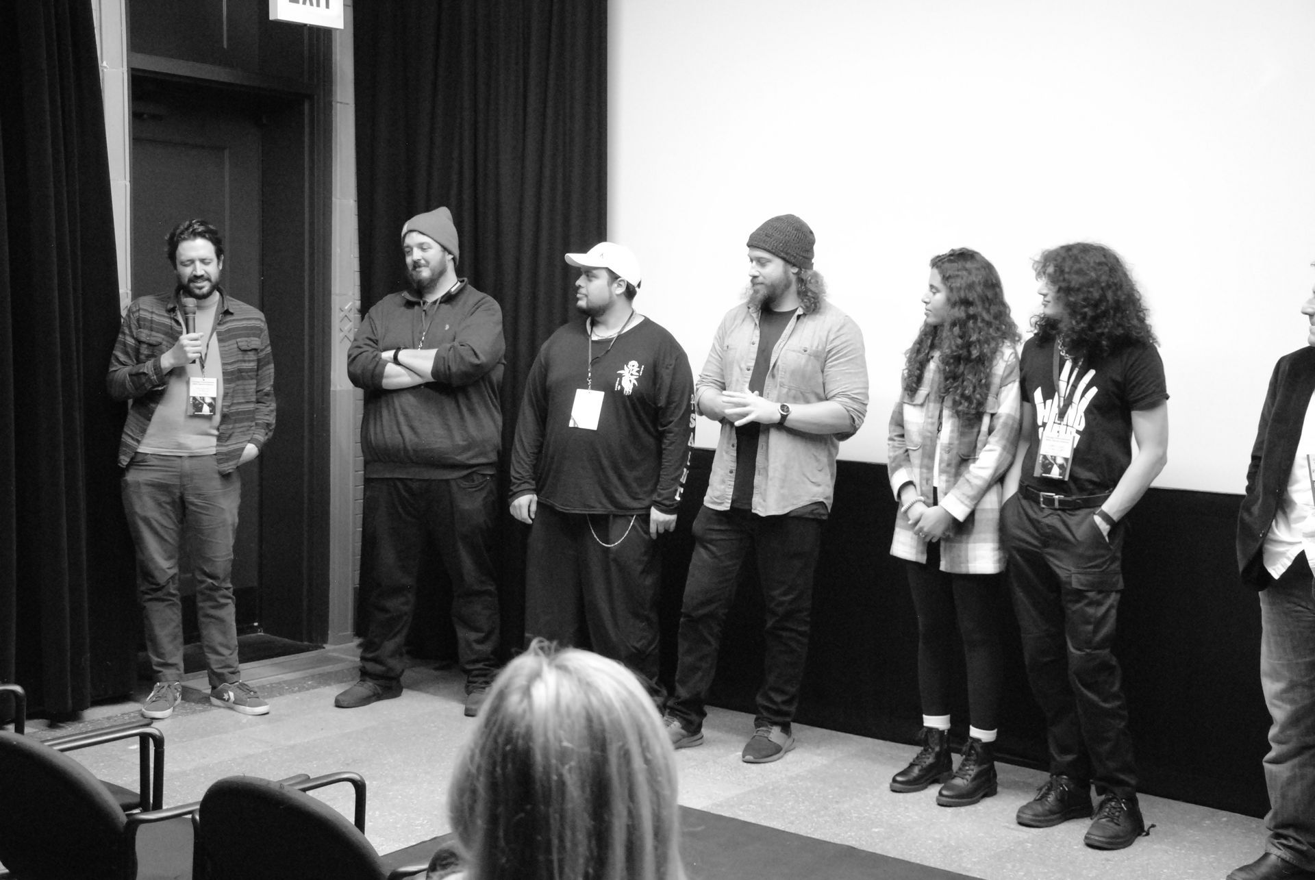 Group of people standing on a stage, talking. Black and white.