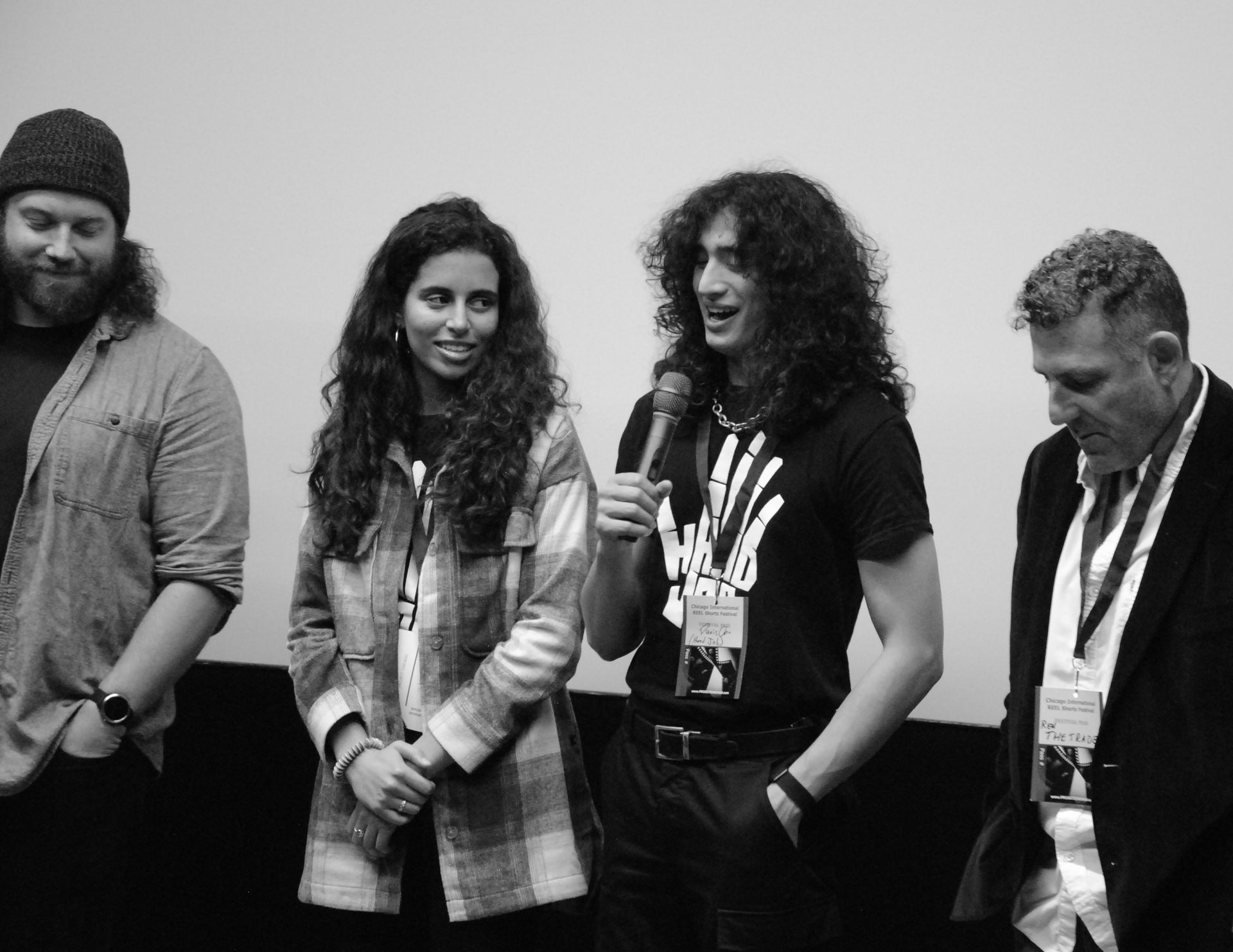 Group of four people on a stage, two with microphones. Black and white photo.