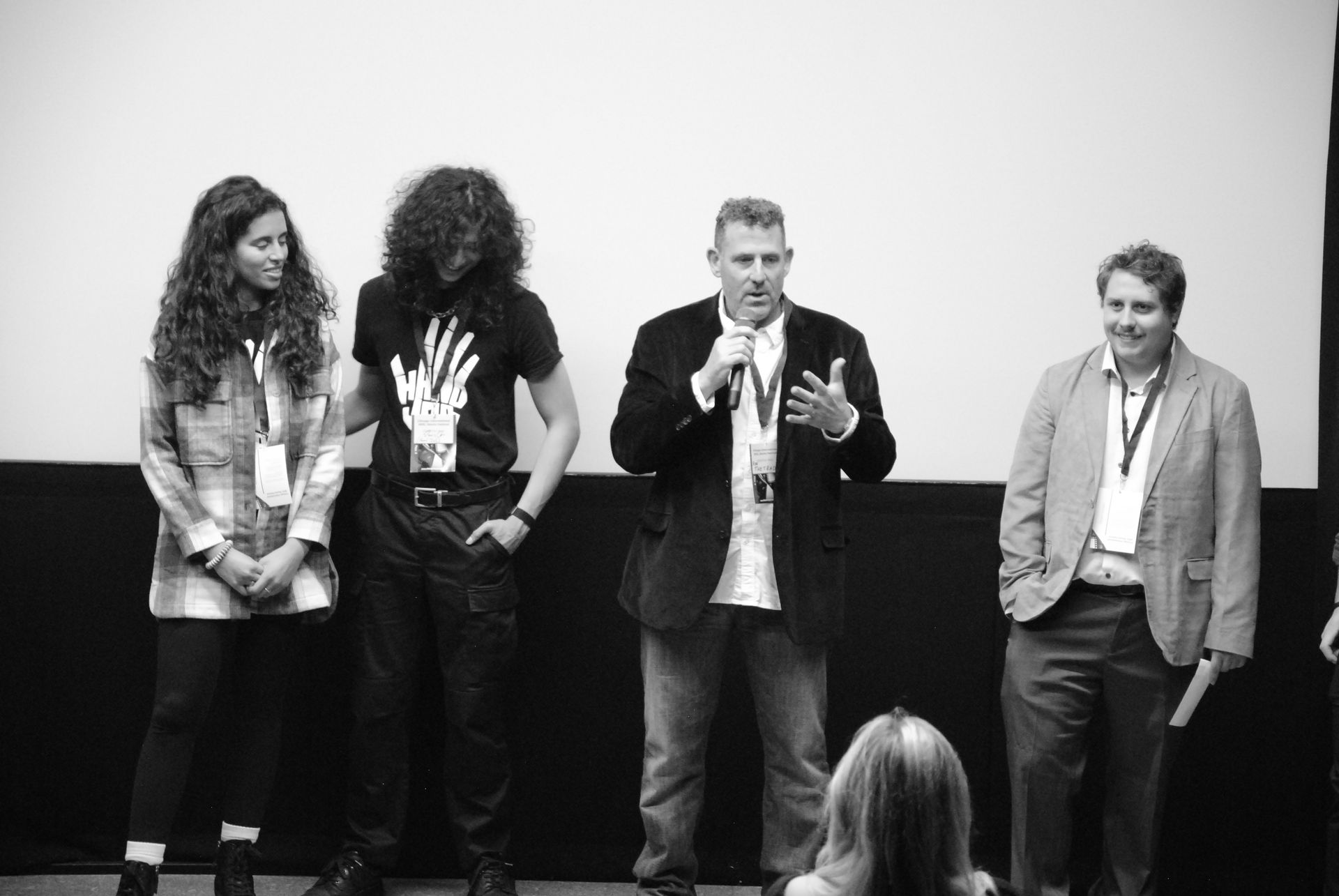 Four people on stage with microphones, at an event. Black and white photograph.