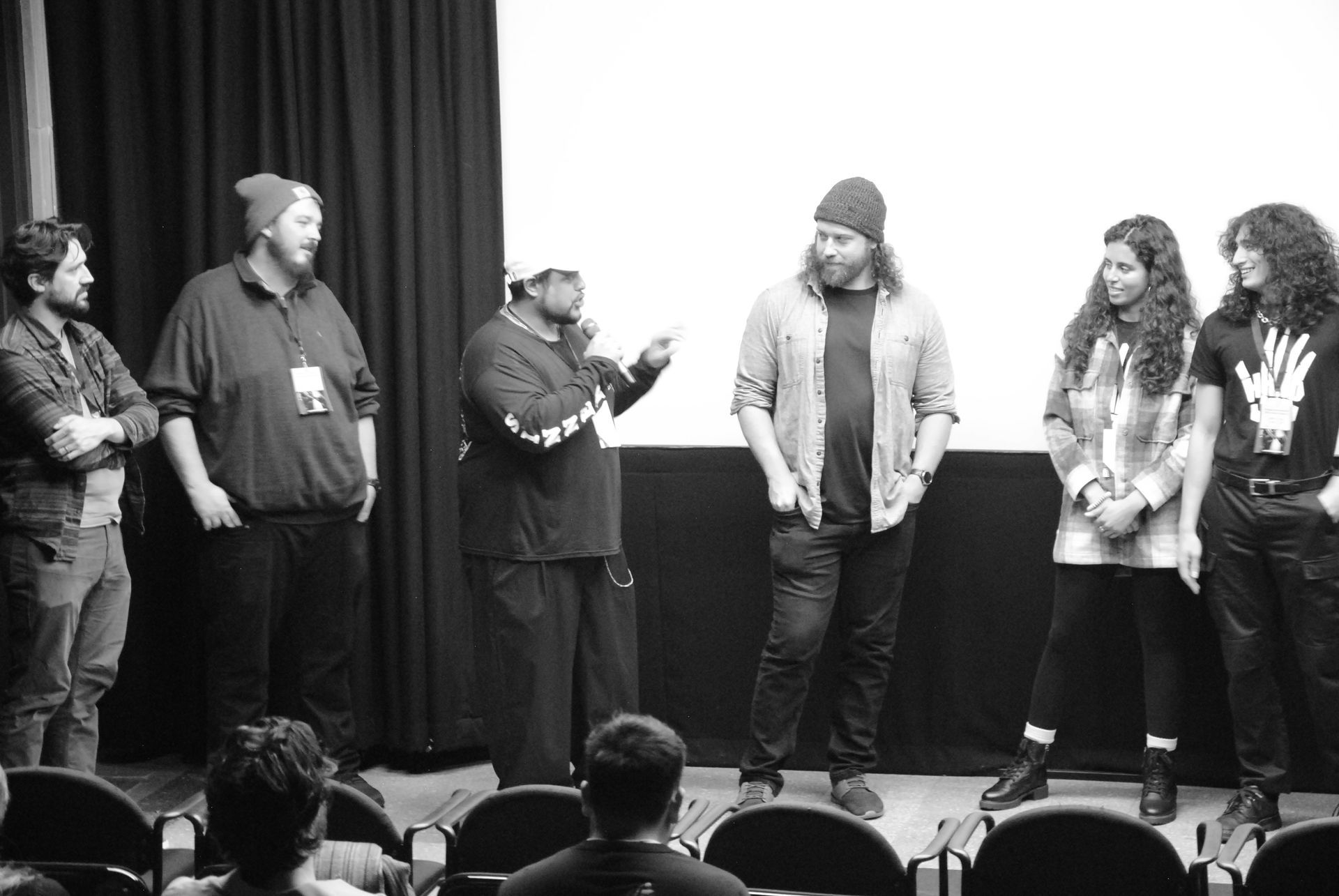 Group of people on a stage in front of a screen, some speaking. Black and white photo.