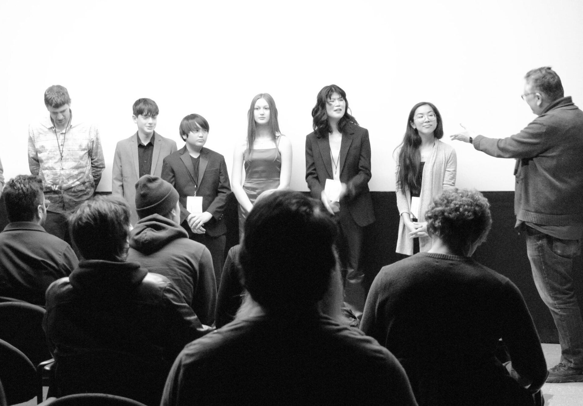 Panel of people on stage, facing audience, with a presenter gesturing towards them.