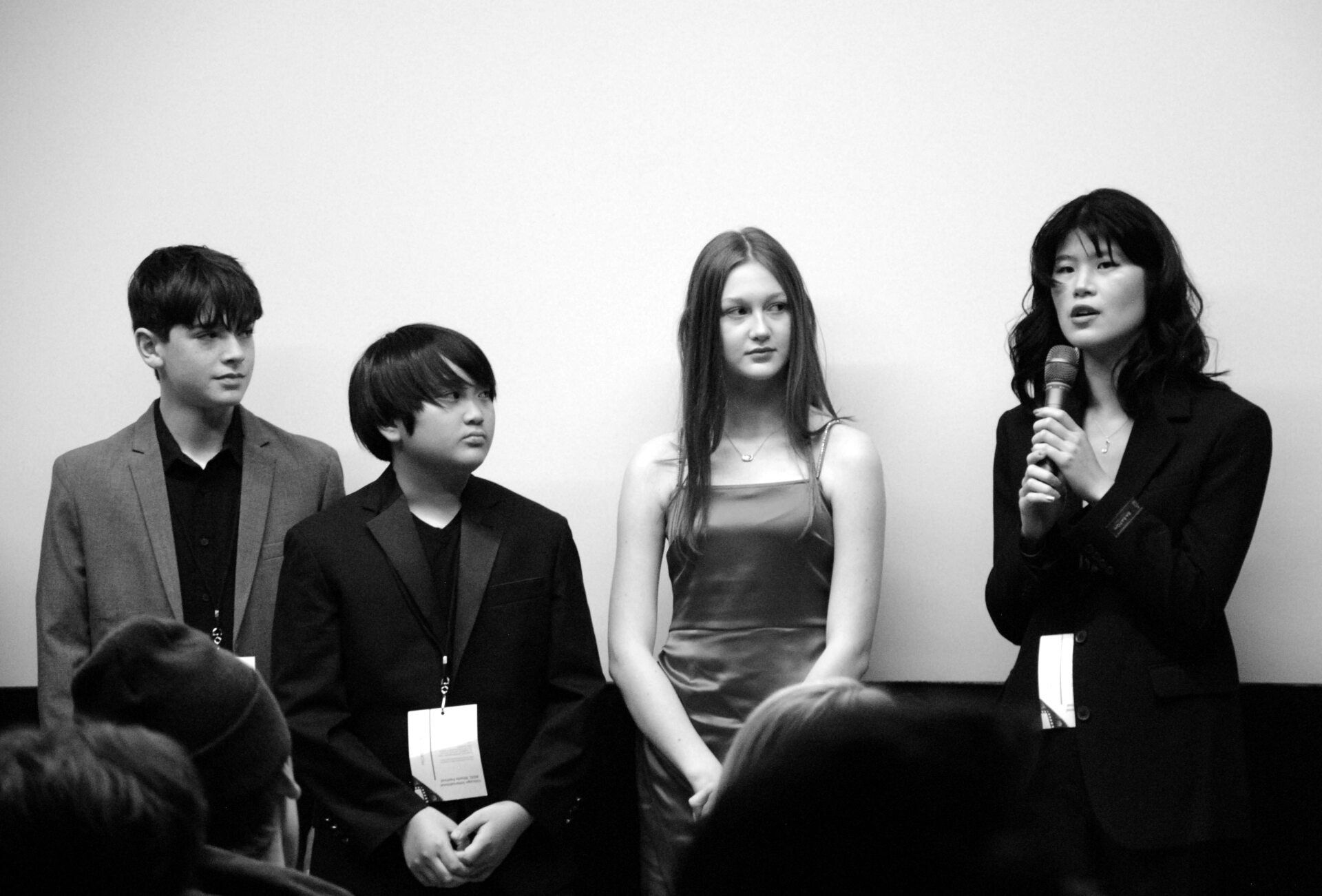 Panel of people at event: three young people, one woman with a microphone, facing the audience.