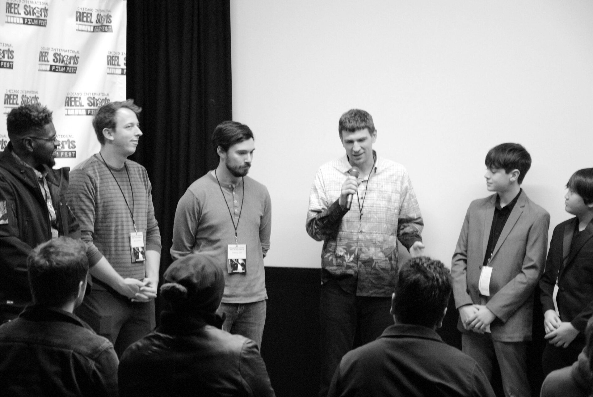 Panel of people at a film festival, one speaking into a microphone, audience in foreground.