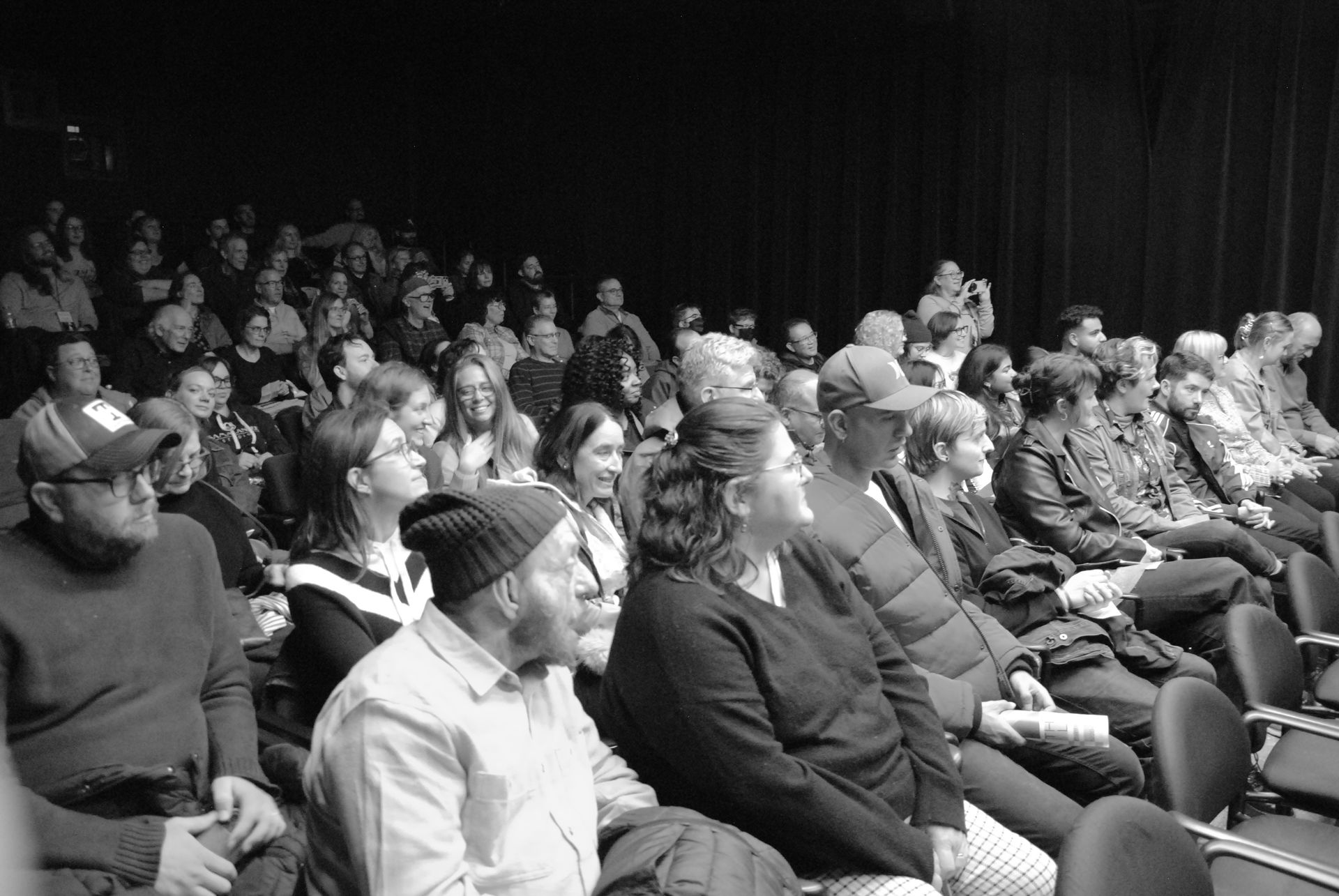 Audience seated in a theater, watching a performance. Black and white photo.