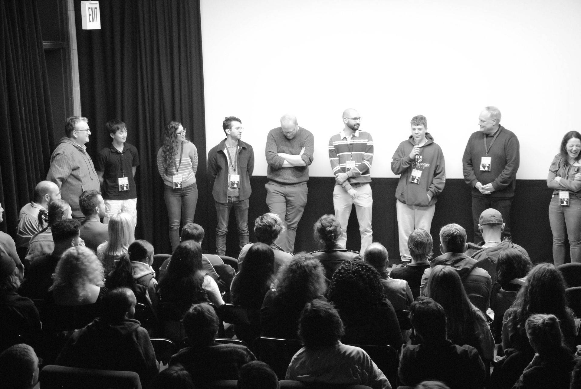 A group of people on a stage with a screen behind them, addressing an audience seated below.