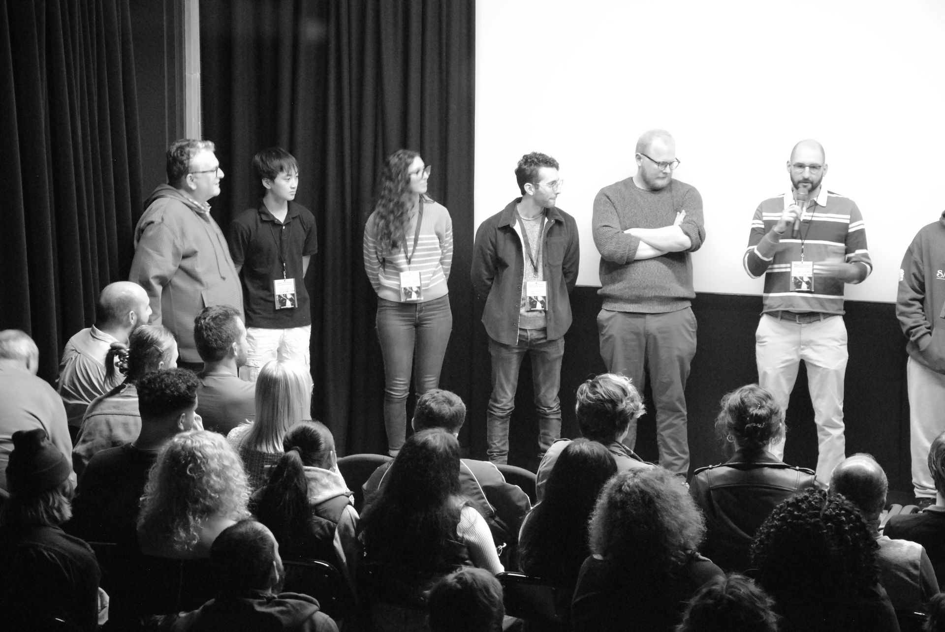 A group of people on a stage, addressing an audience seated in a theater. Black and white photo.