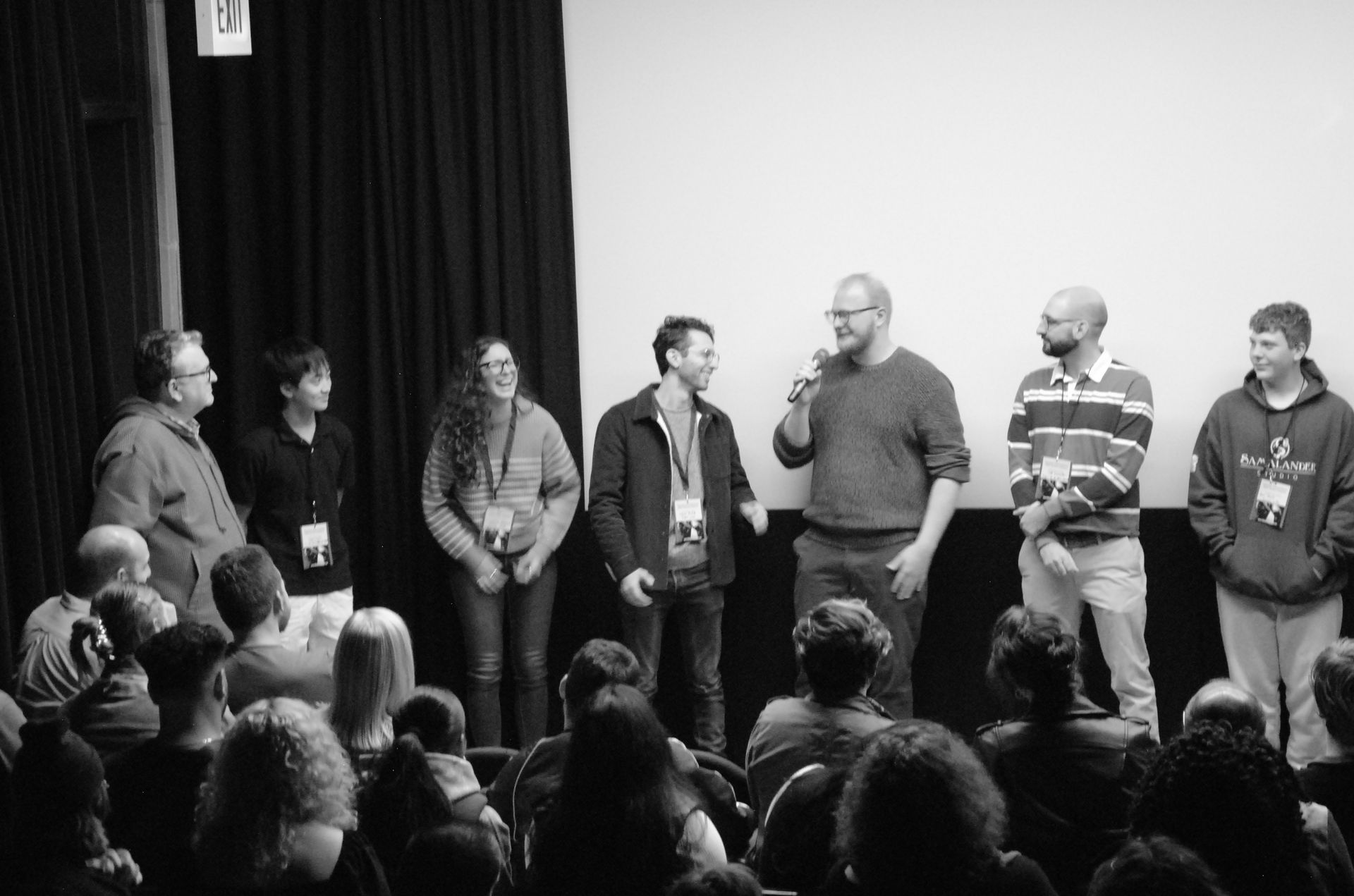 Panel of people on a stage speaking to an audience in a theater. Black and white.