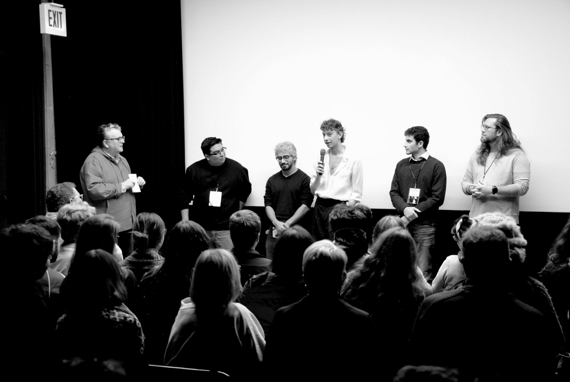 Panel of six people on stage, answering questions in front of an audience and blank movie screen.