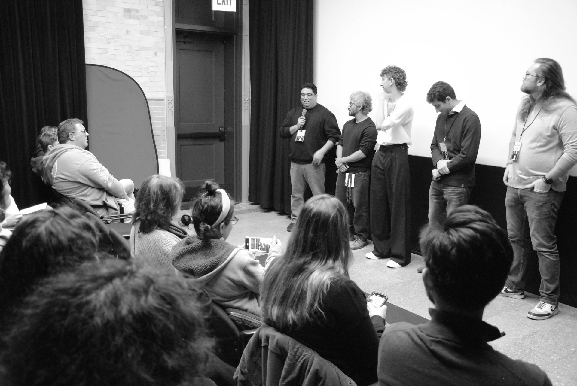Panelists on stage speaking to an audience in a theater. Black and white photograph.