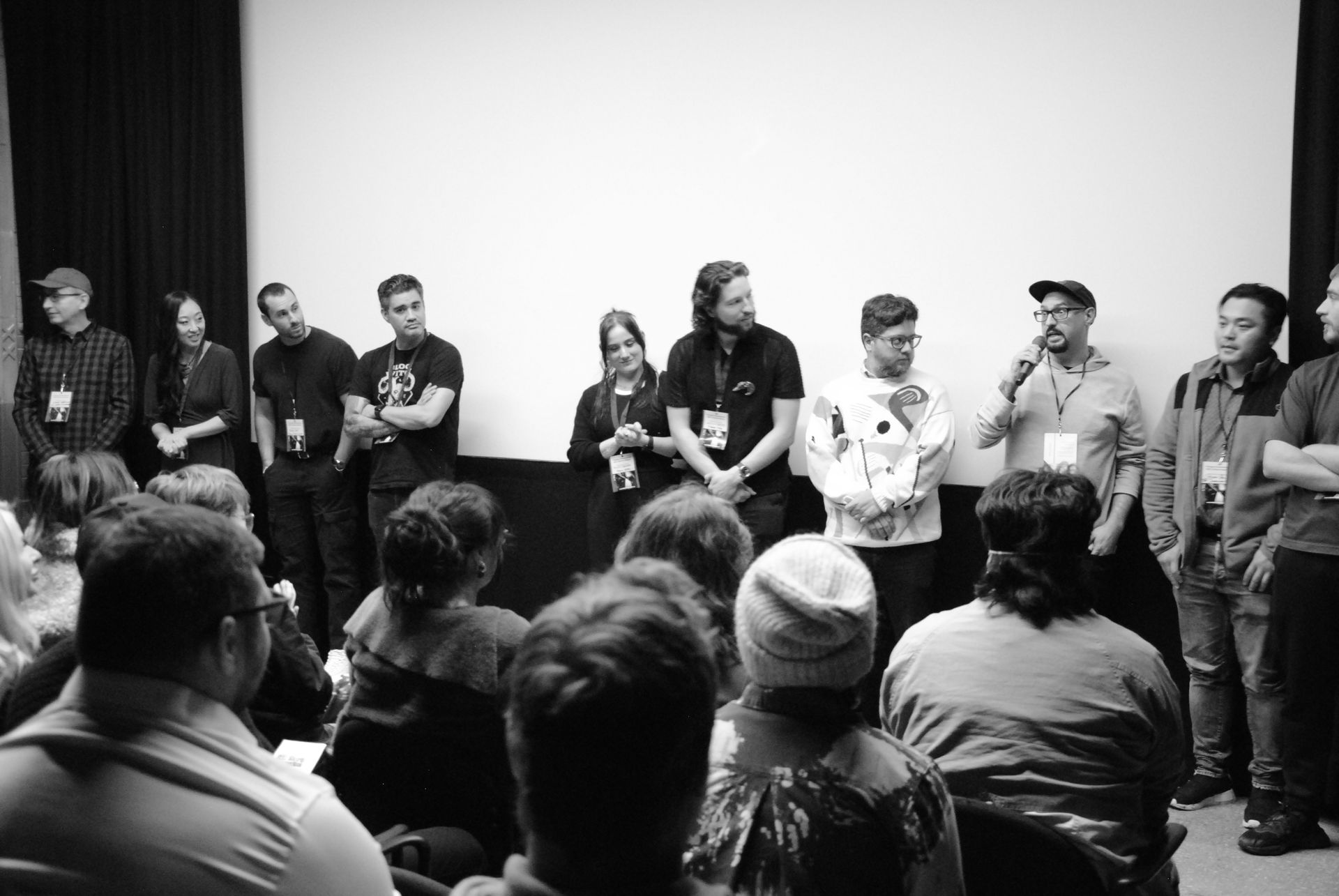 Panelists on stage in front of an audience; a screen is behind them, people hold microphones.