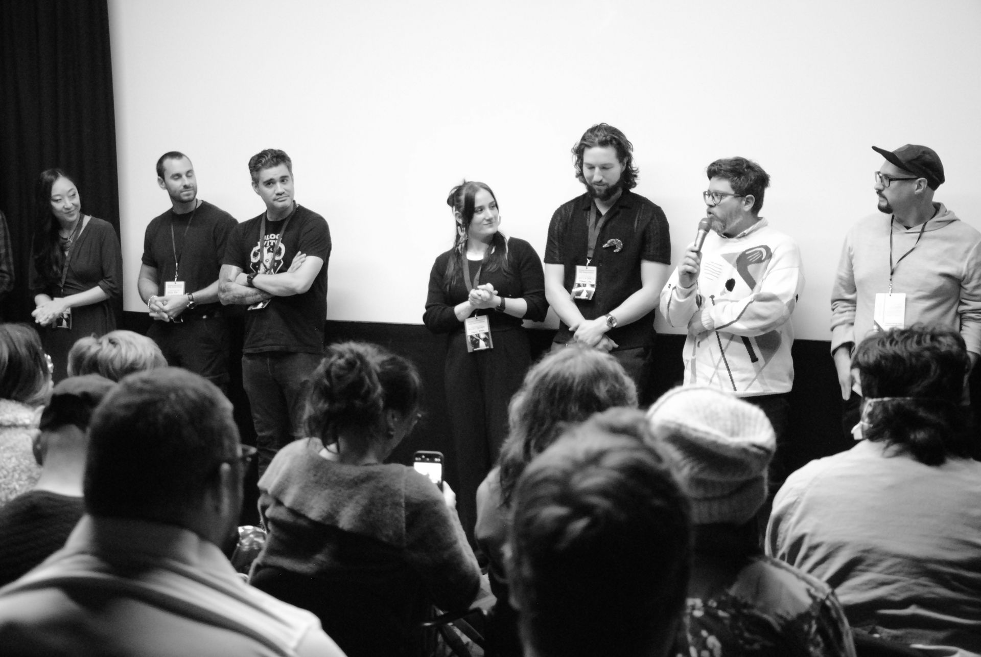 Panel of filmmakers at an event, speaking to an audience in front of a screen. Black and white.