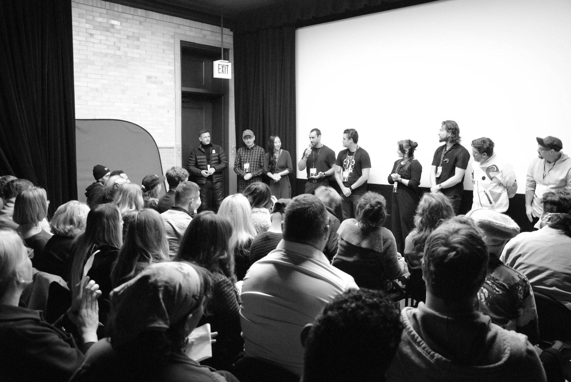 Audience at a Q&A with a panel of people onstage in a theater. Black and white photo.