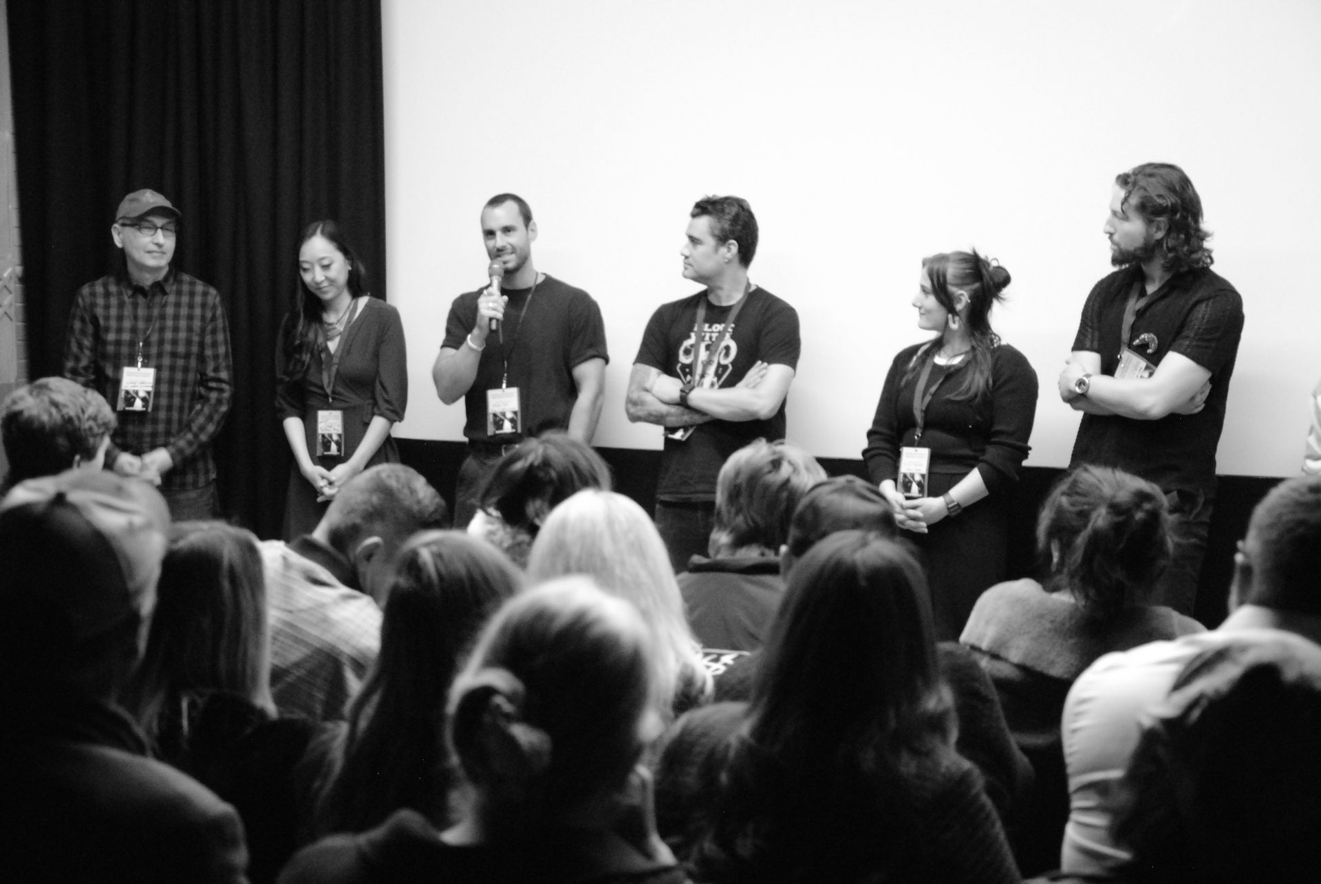 Panel of people on a stage addressing a seated audience in front of a screen, black and white.