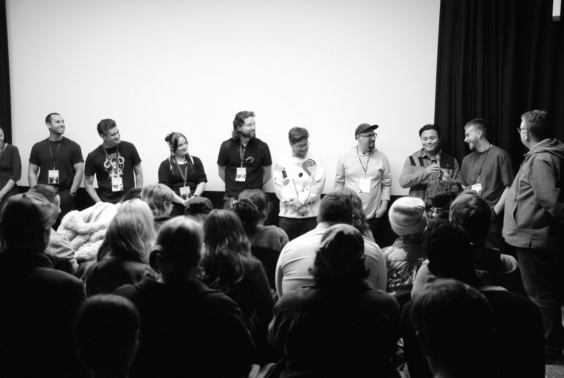 Panel of people on a stage in front of an audience, all wearing badges. Black and white photo.