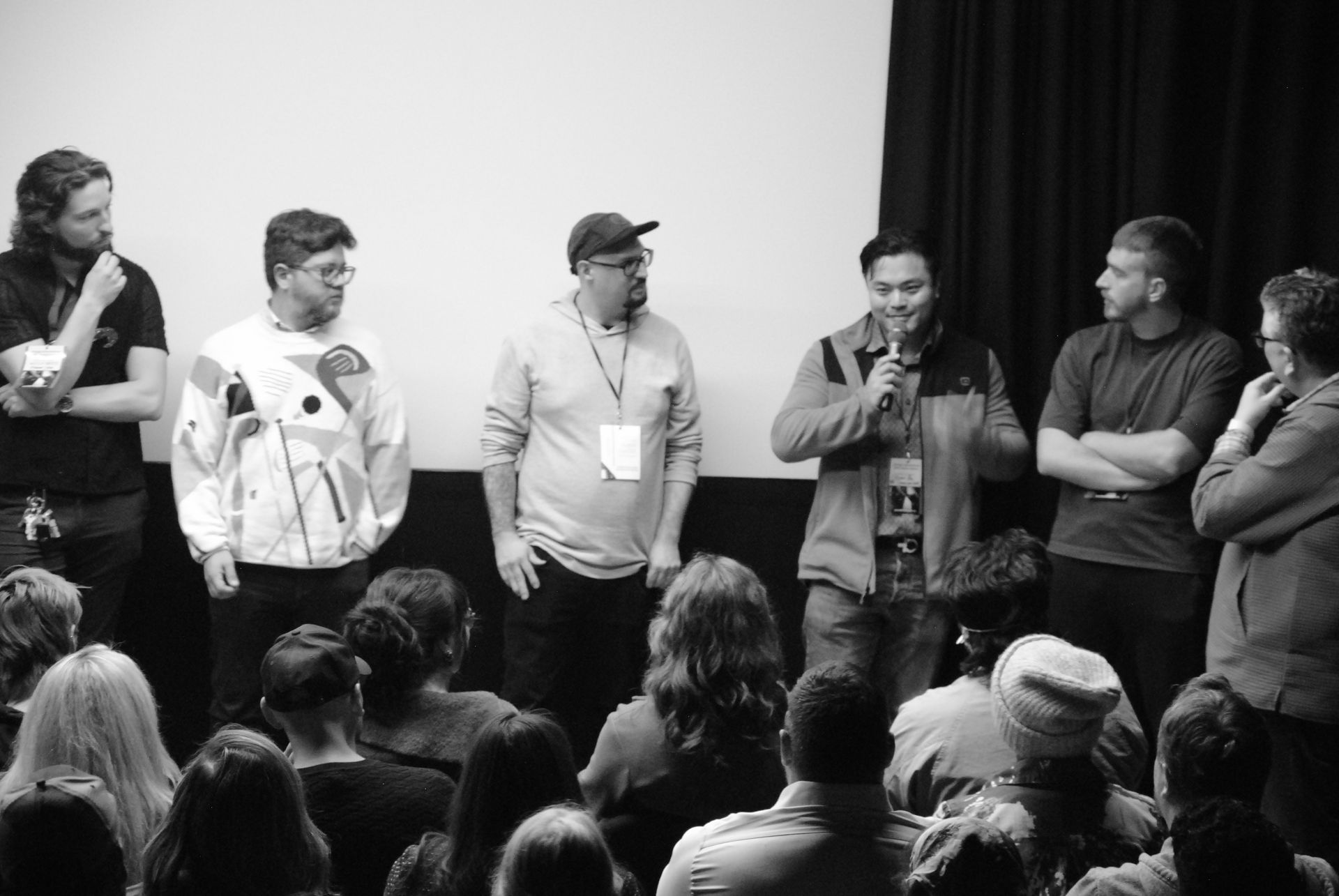 Group of men on a stage, speaking to an audience. Black and white.