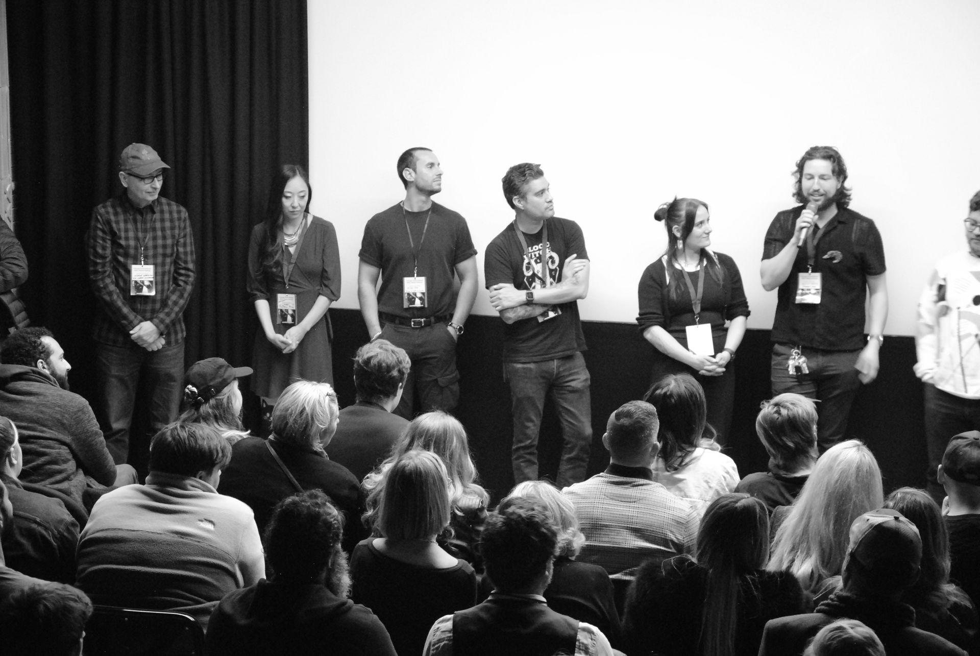 Panel of people on stage in front of an audience, speaking during an event. Black and white.