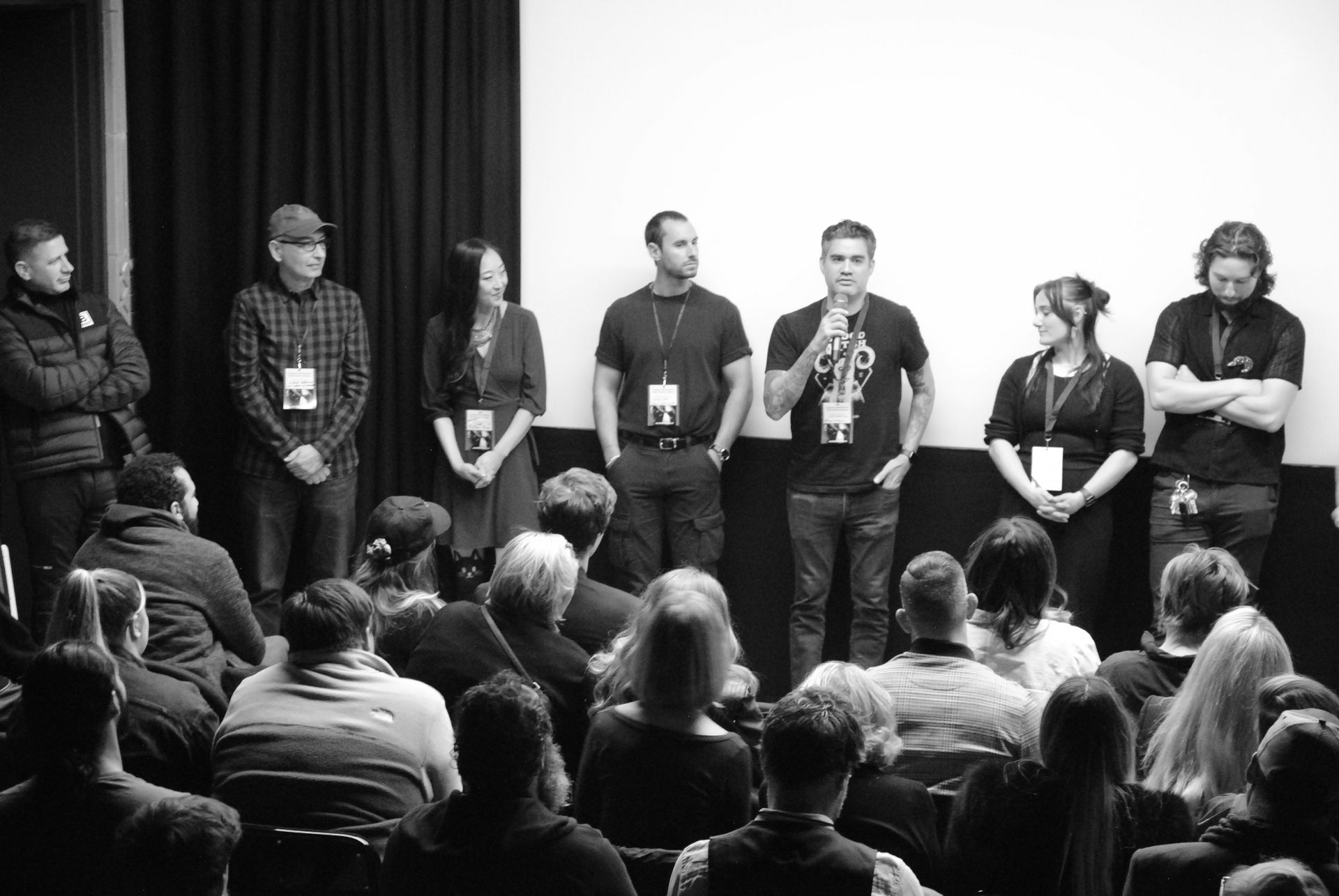 Panel of people on stage speaking to an audience in a theater. Black and white.