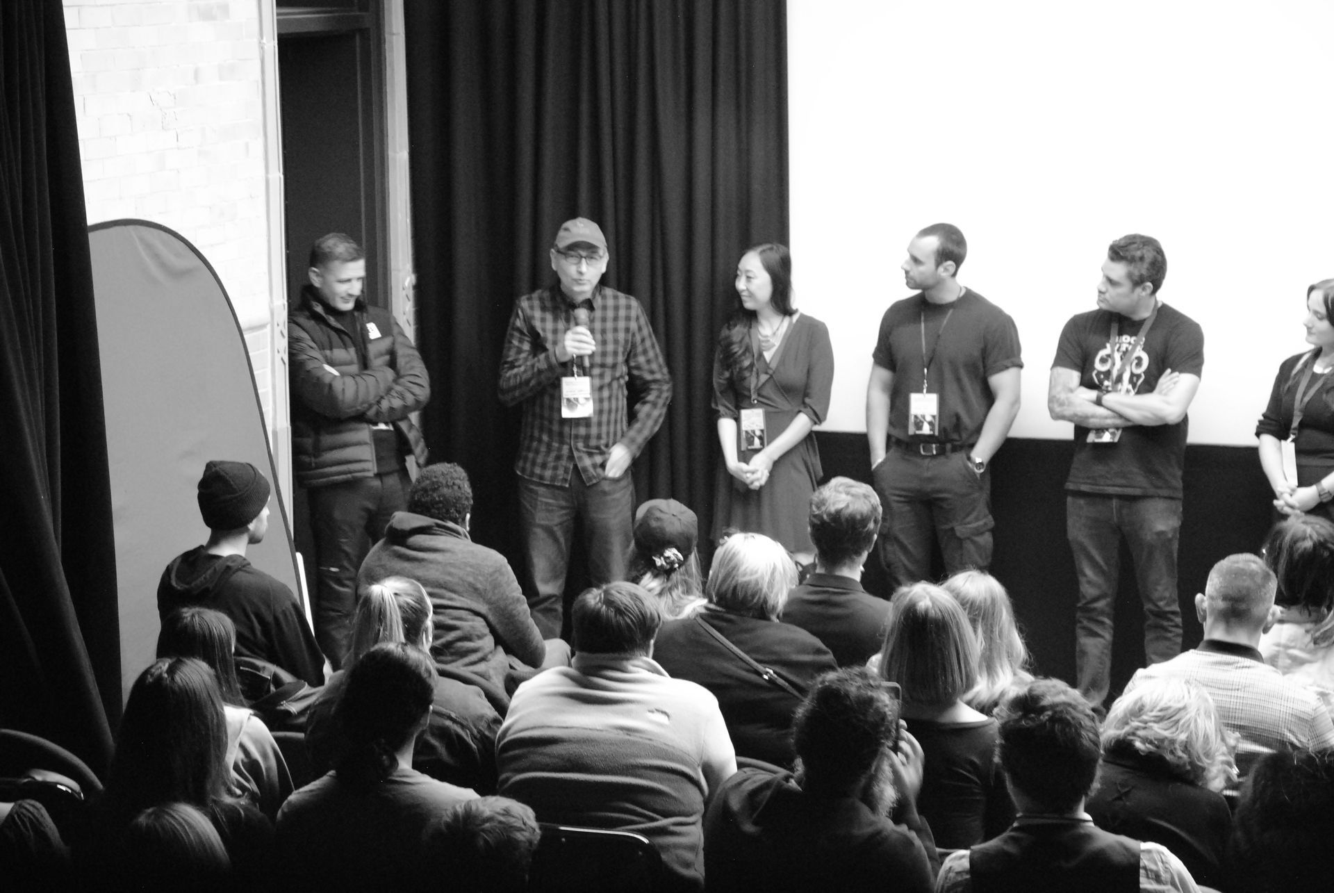 A panel of people on a stage speaks to an audience in a theater. Black and white.