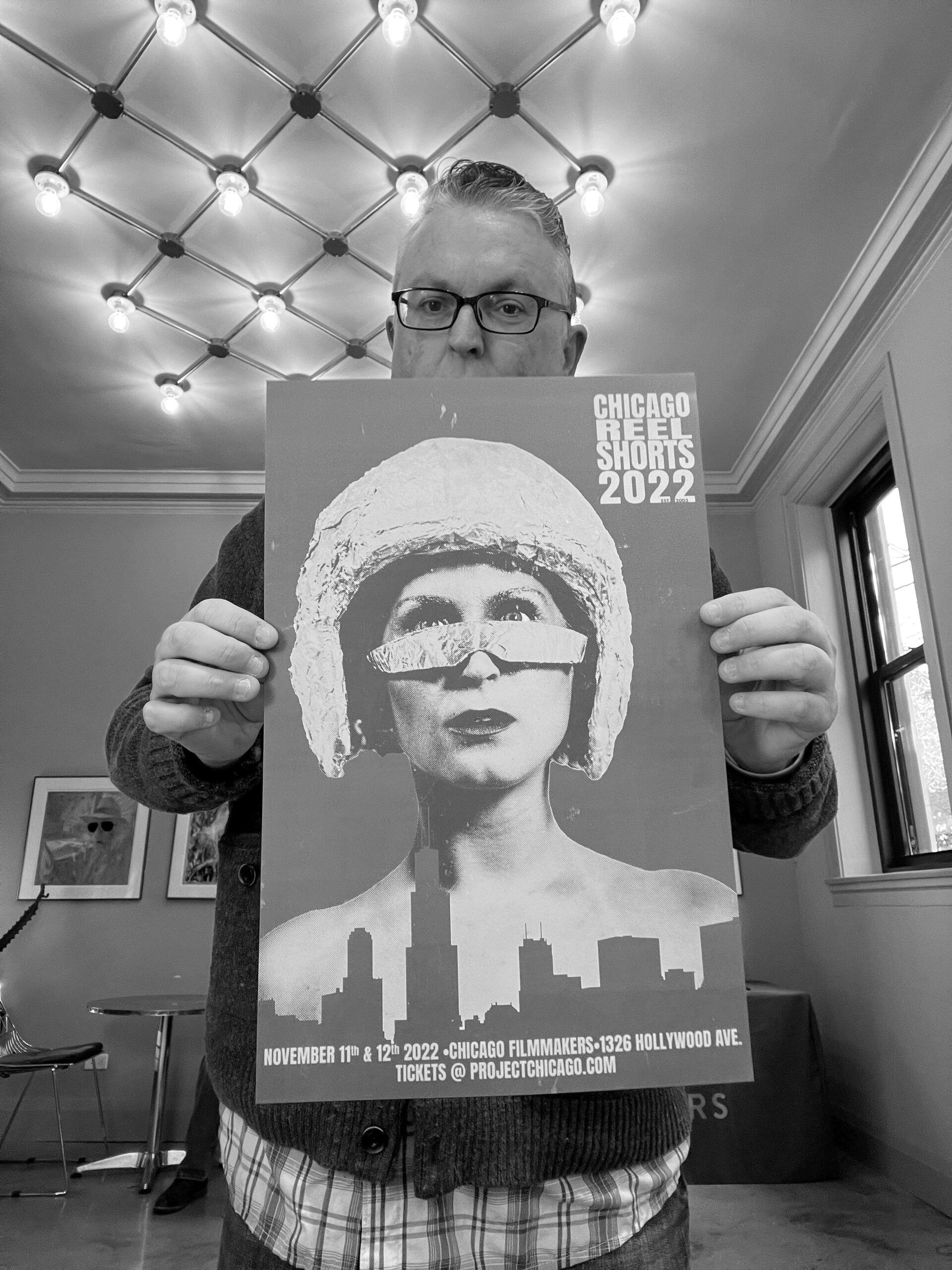 Man holds a Chicago Film Fest 2022 poster with a woman wearing a helmet and sunglasses; city skyline visible.