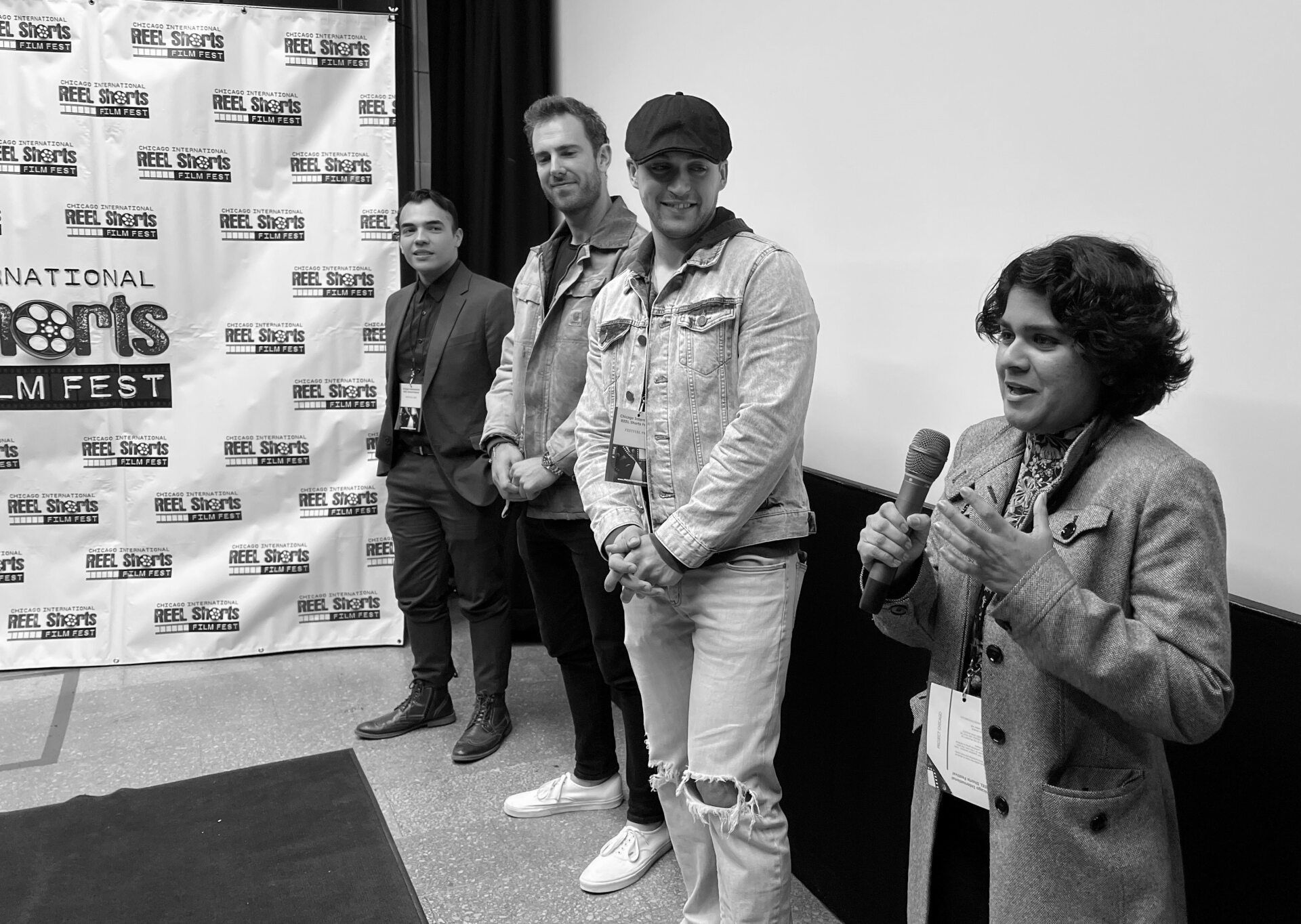 Four people stand in front of a backdrop. One woman holds a microphone. All appear at a film festival.