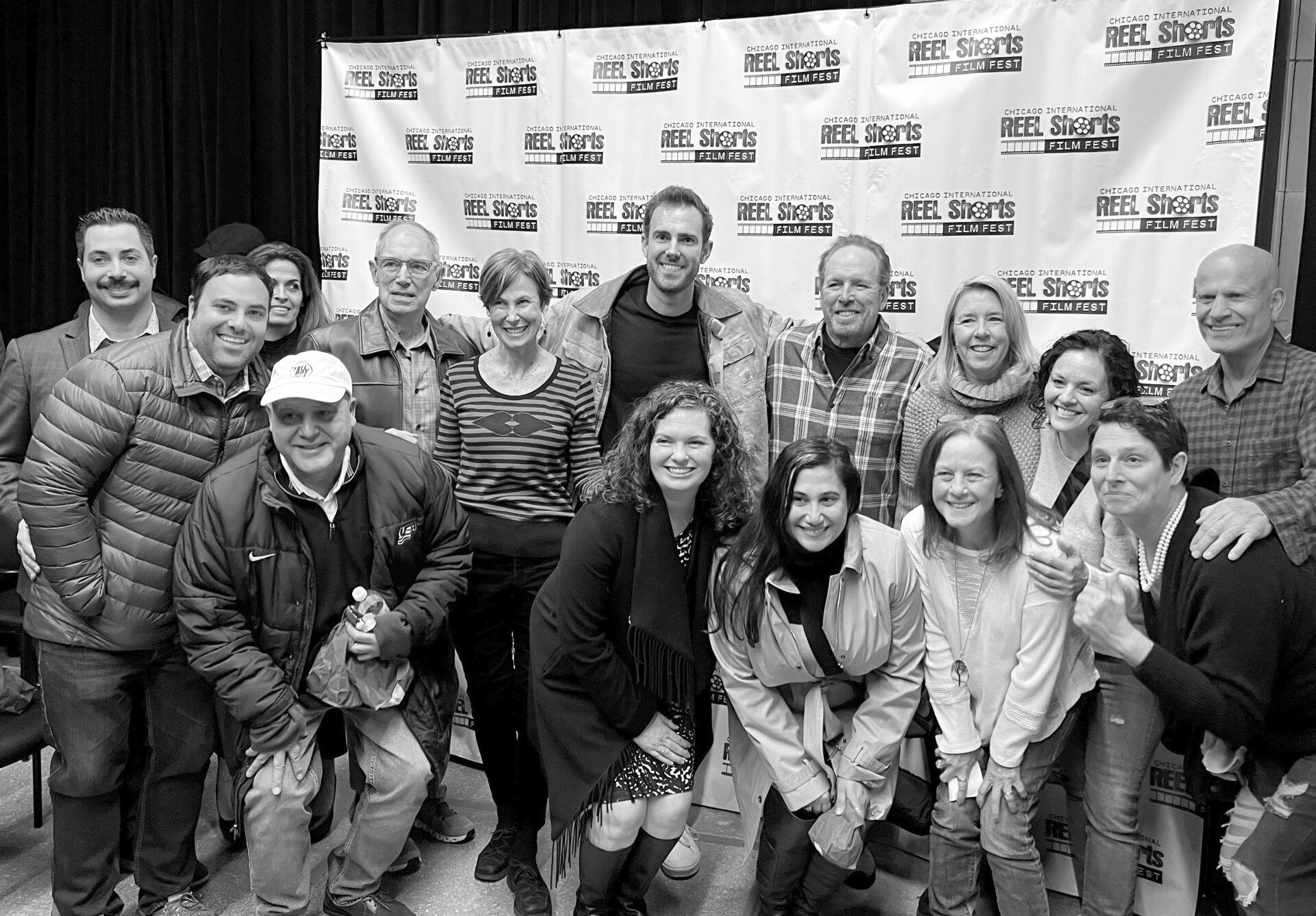 Group of people smiling at the camera in front of a banner, indoors.
