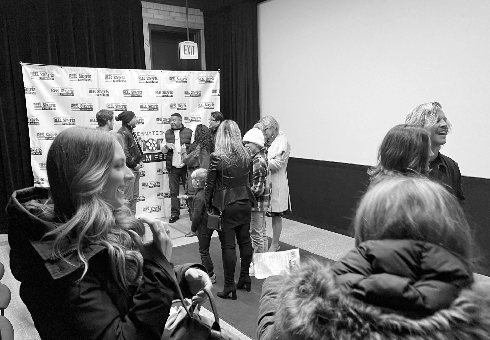 People at an event, posing near a backdrop. Indoor setting. Black and white photo.