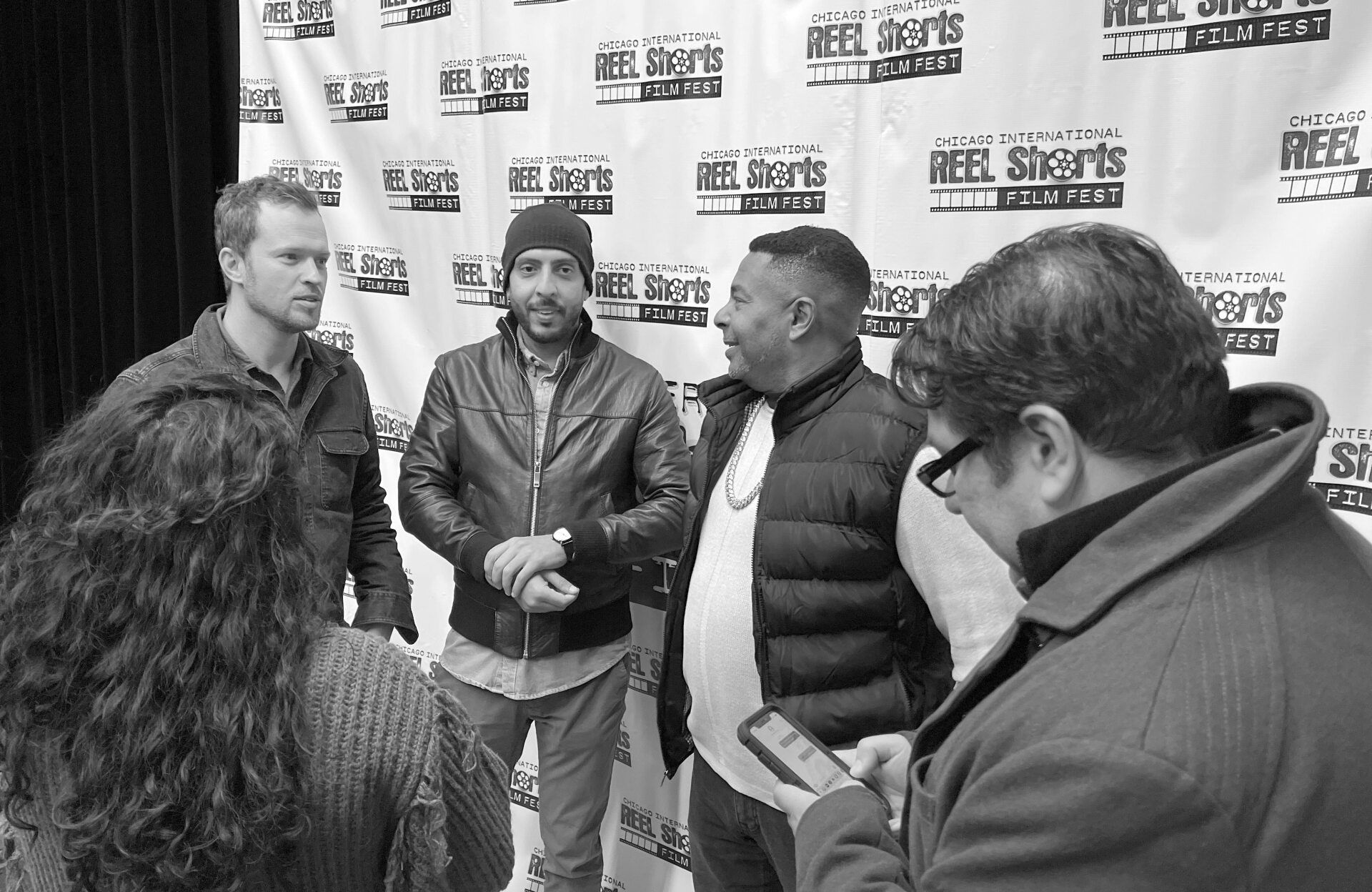People pose at a film festival. Three men stand by a backdrop, being photographed.