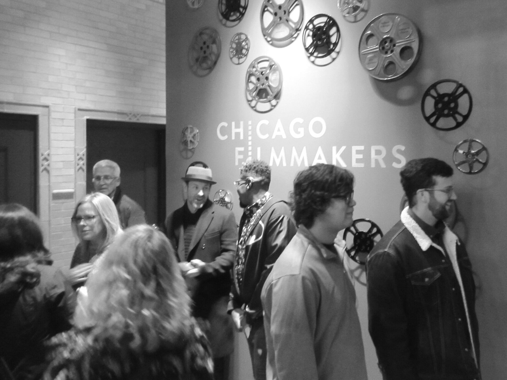 People gathered at the Chicago Filmmakers organization, next to a wall decorated with film reels.