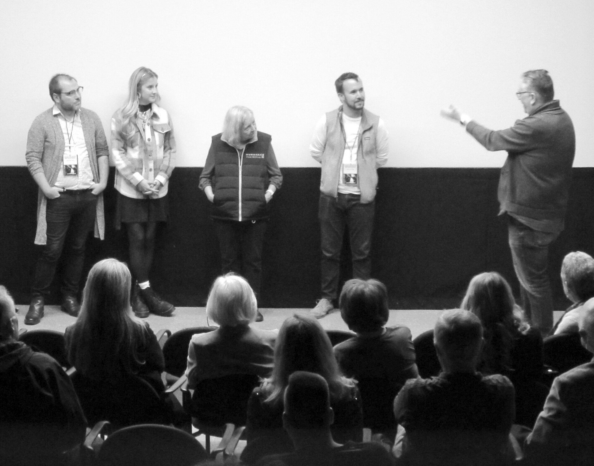 Panelists on stage at a film screening; audience seated in front. Black and white photo.