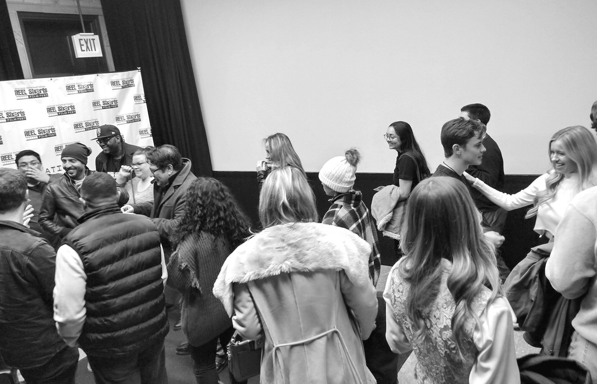 People interacting in a theater. Some are on a panel, others in the audience. Black and white photo.