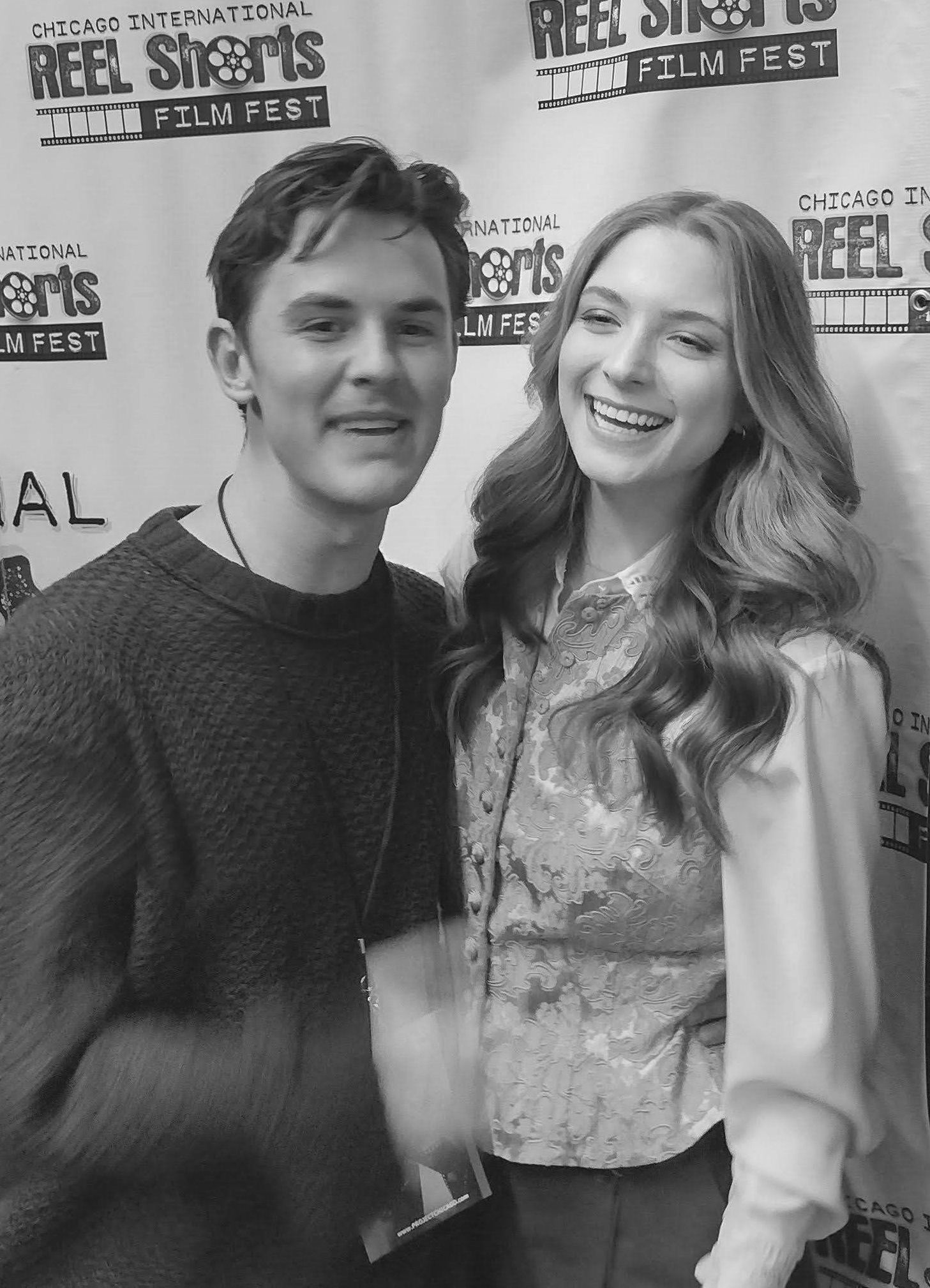 Young man and woman smiling, posing together in front of a film festival backdrop.