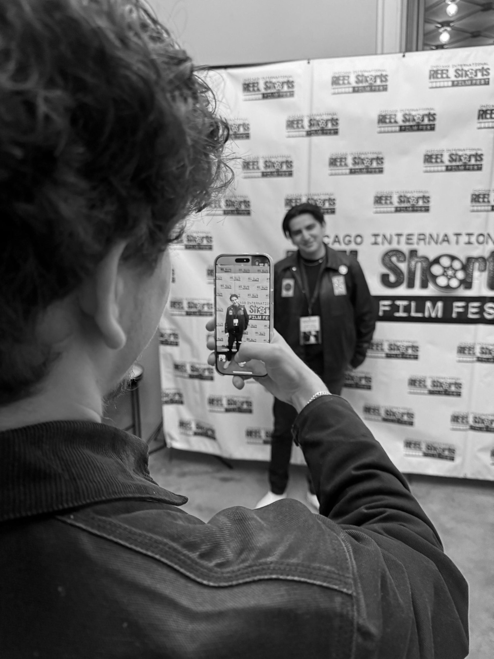 Person taking photo of another person at a film festival. Both are in front of a backdrop.