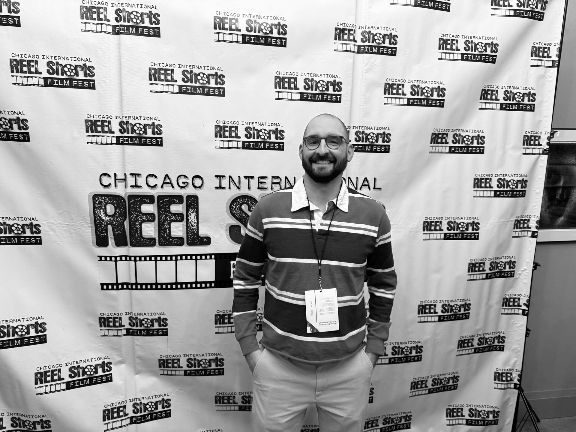 Man with glasses, at the Chicago International Reel Shorts film festival. Standing in front of a festival backdrop.