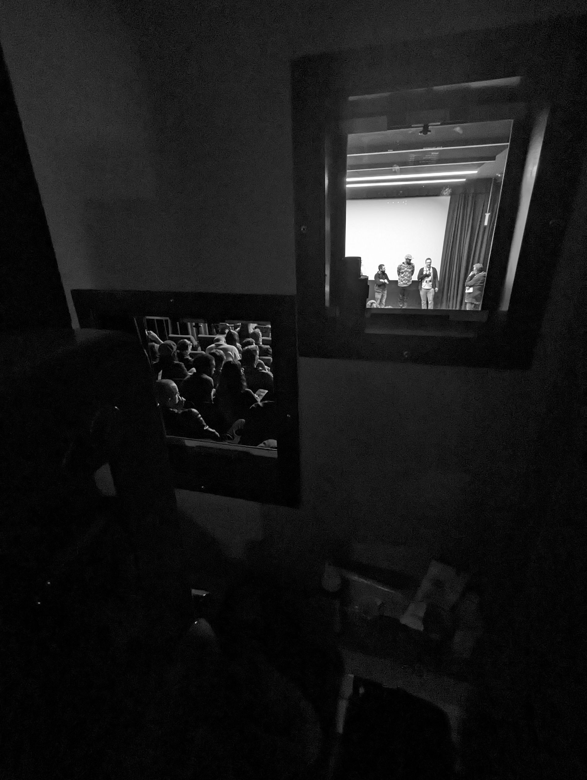 Audience viewing a stage performance through two windows in a dark room.