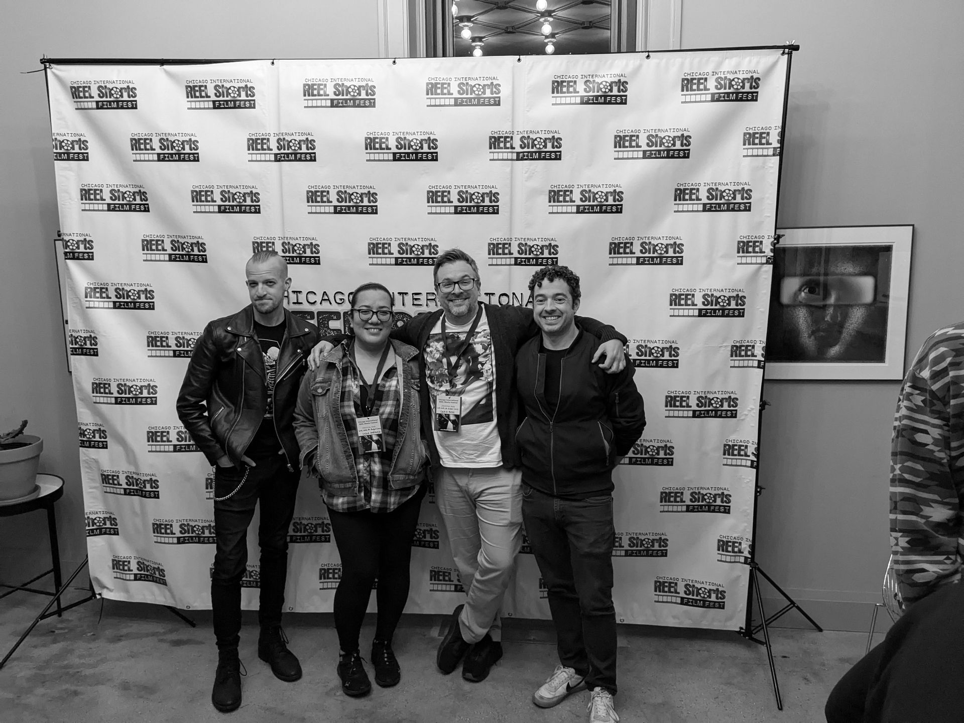 Four people pose for a photo in front of a backdrop with logos at an event.