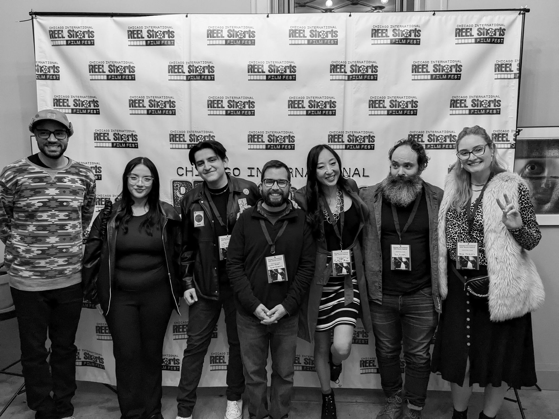 Group poses in front of a backdrop at a film festival. People smiling, wearing lanyards. Black and white.