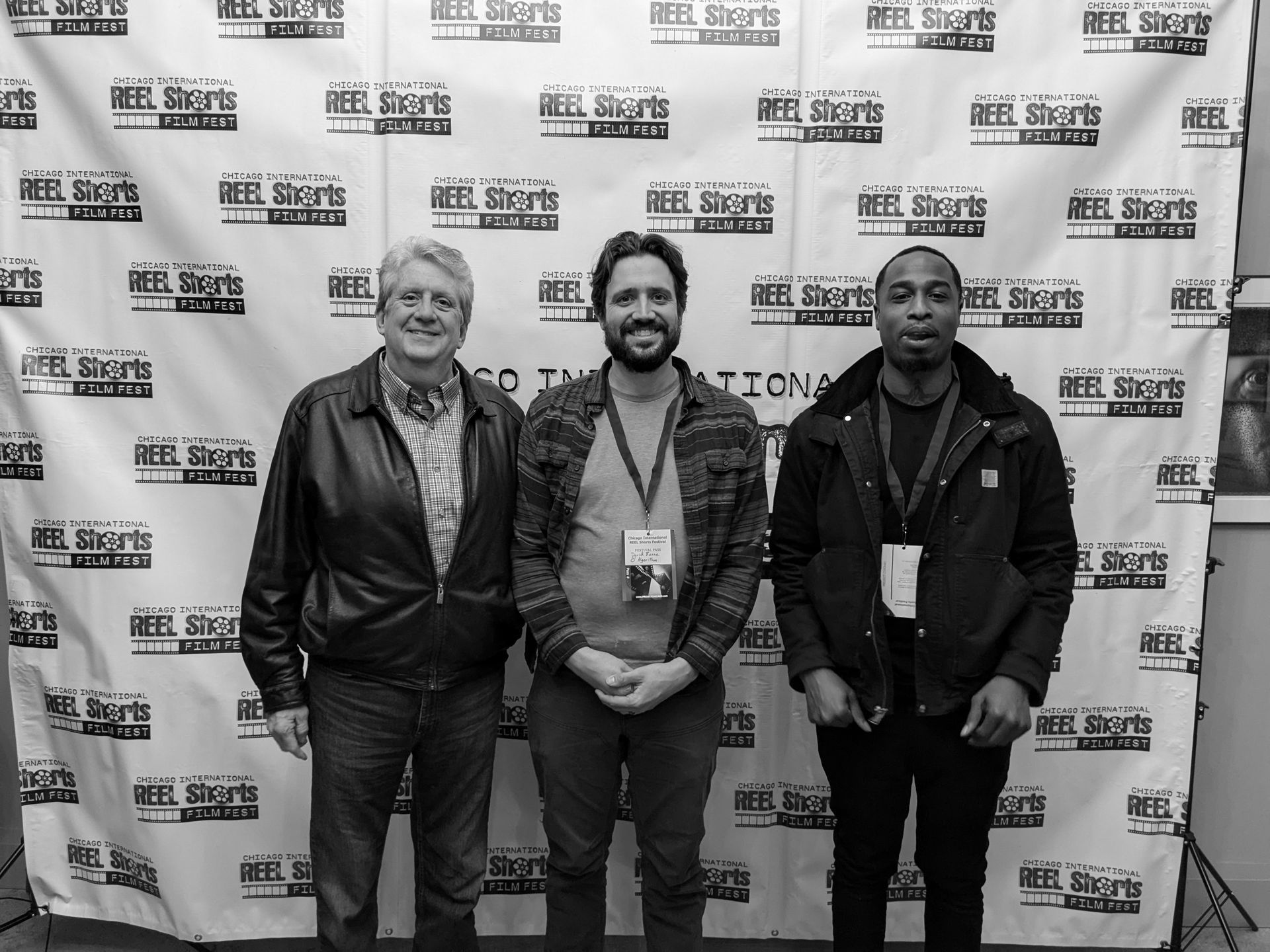 Three men standing in front of a banner at a film festival, smiling.