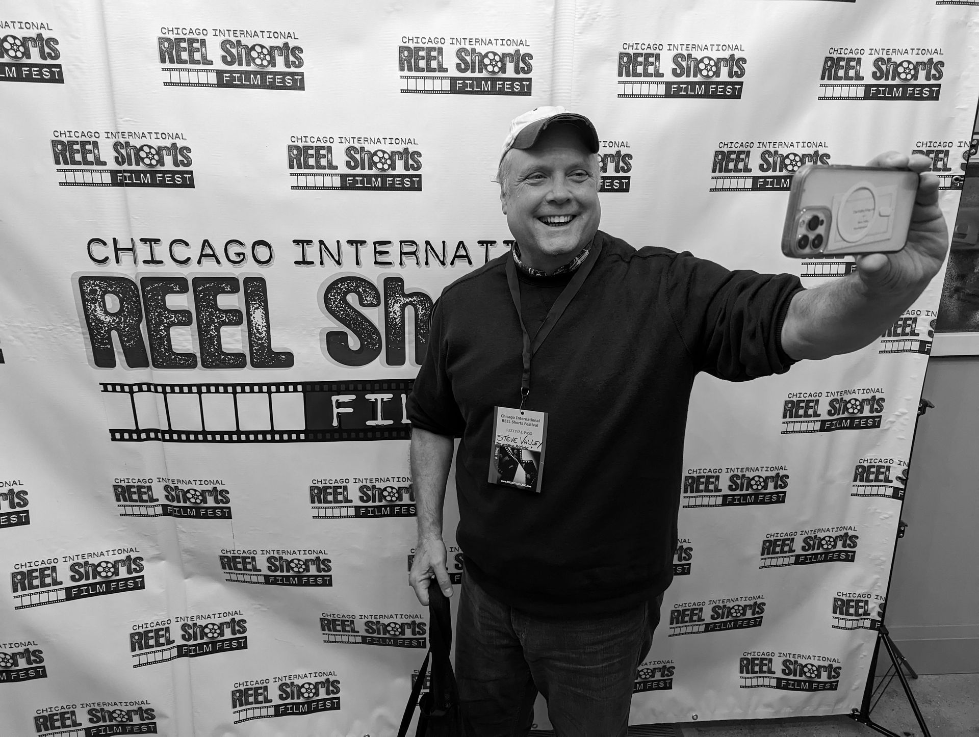 Man smiling, taking selfie with a film festival backdrop.