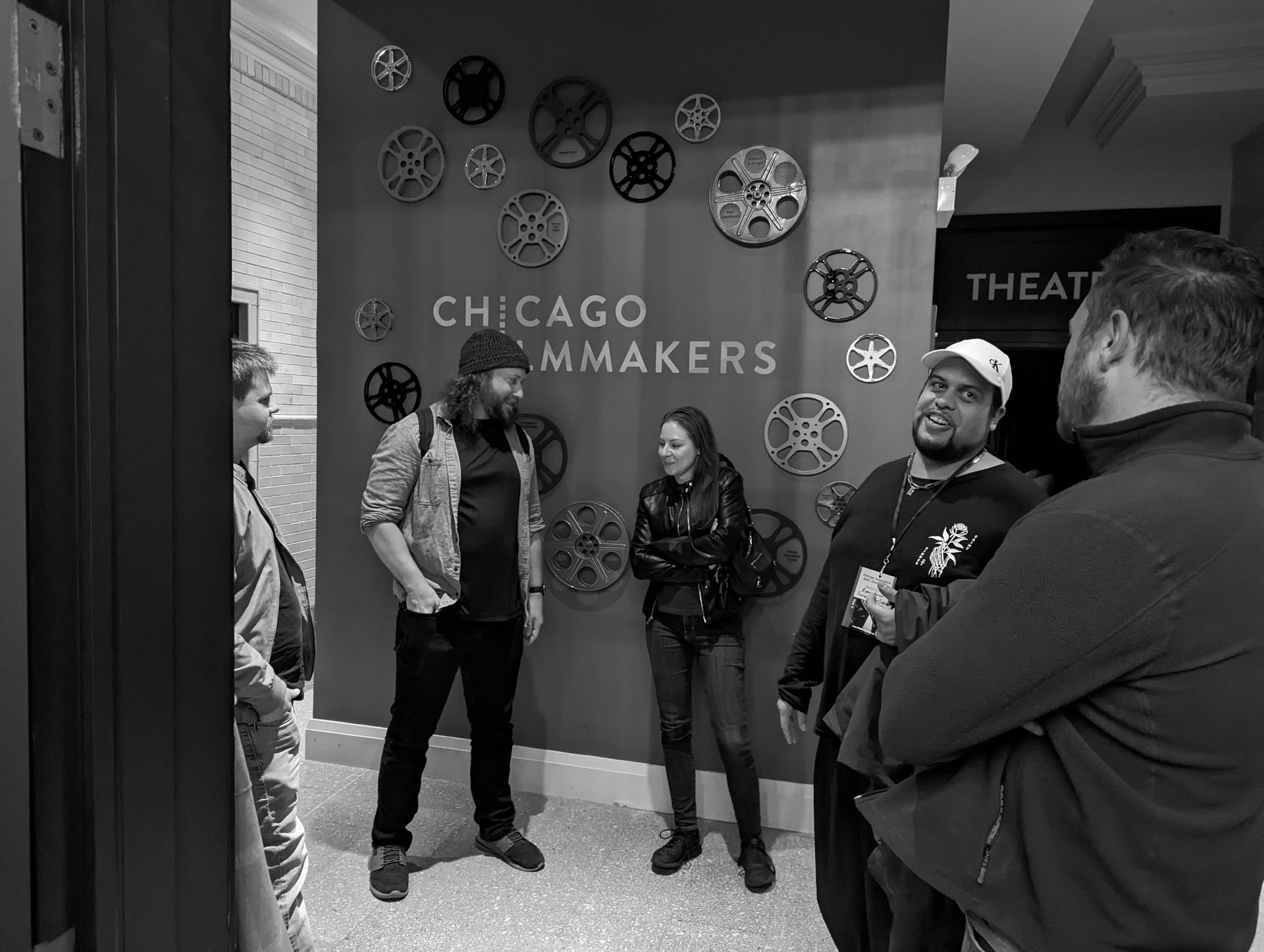 People at a Chicago Filmmakers event pose near a wall decorated with film reels; Theater sign visible.