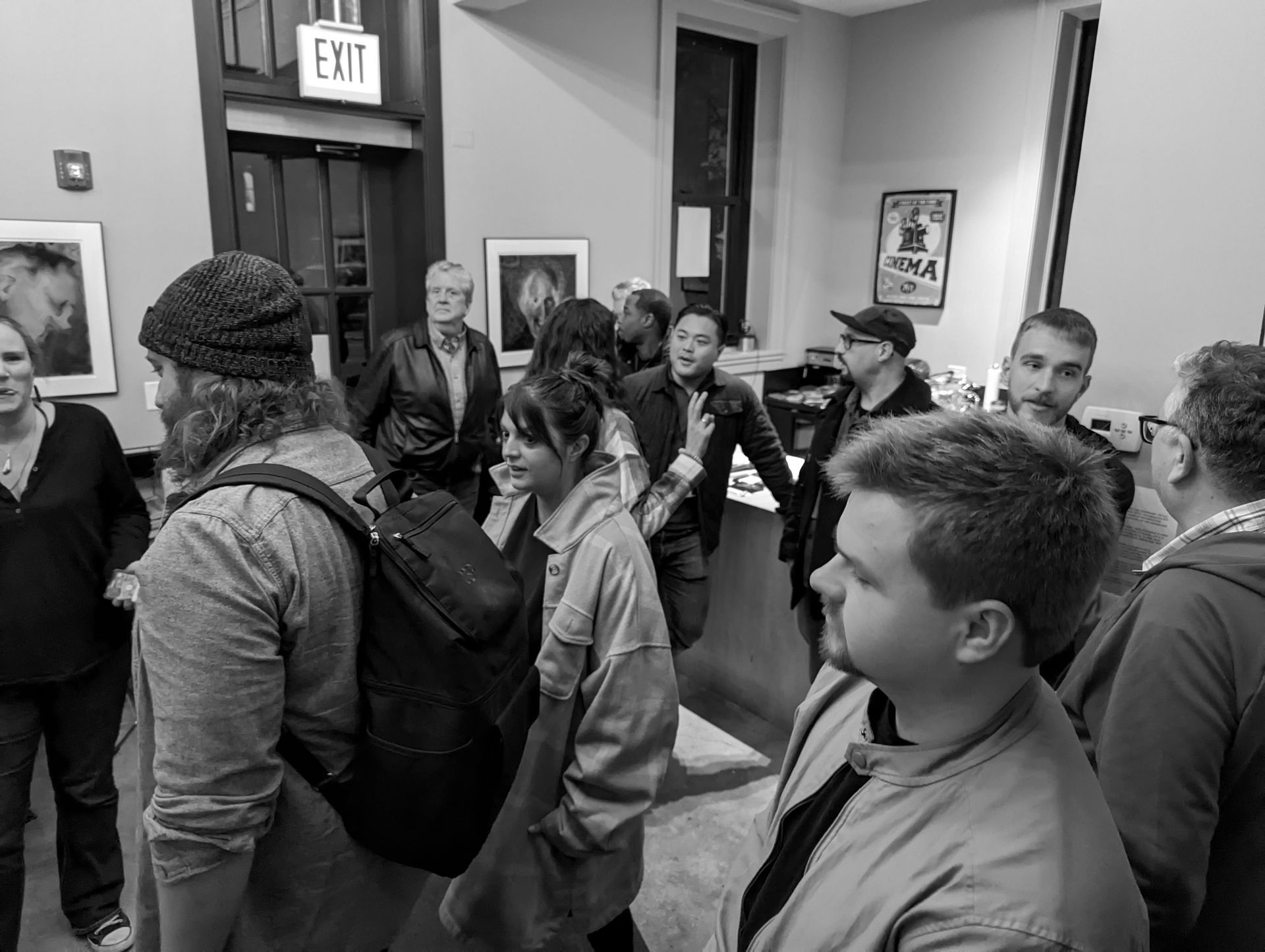People gathered indoors near an exit door. Some are smiling, others look forward. Artwork on the walls.