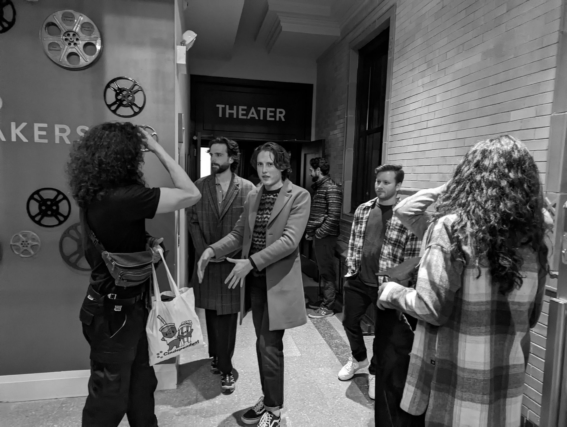 People in an interior hallway pose near a theater entrance. Black and white.