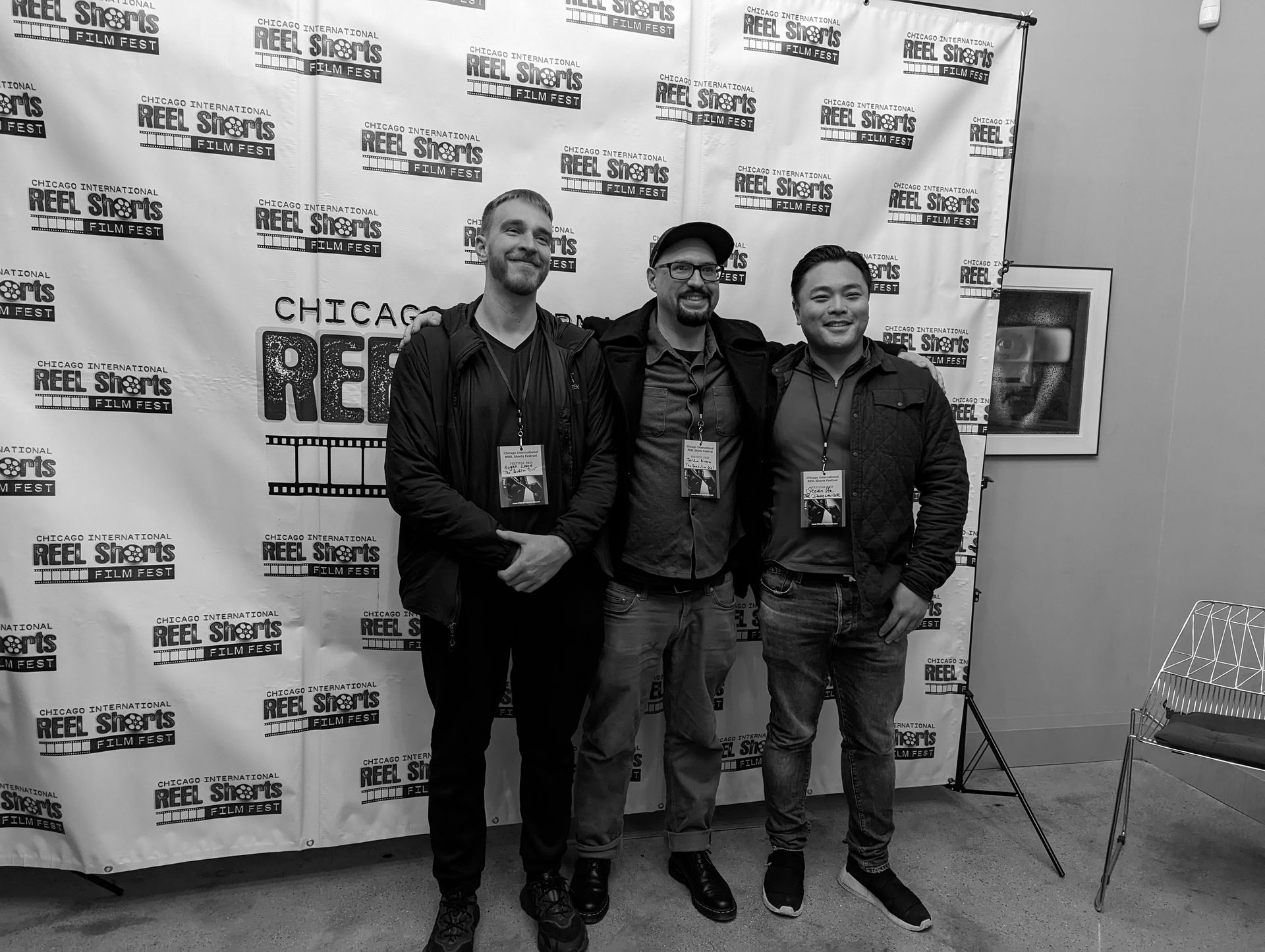 Three men stand smiling in front of a white backdrop at a Chicago event.