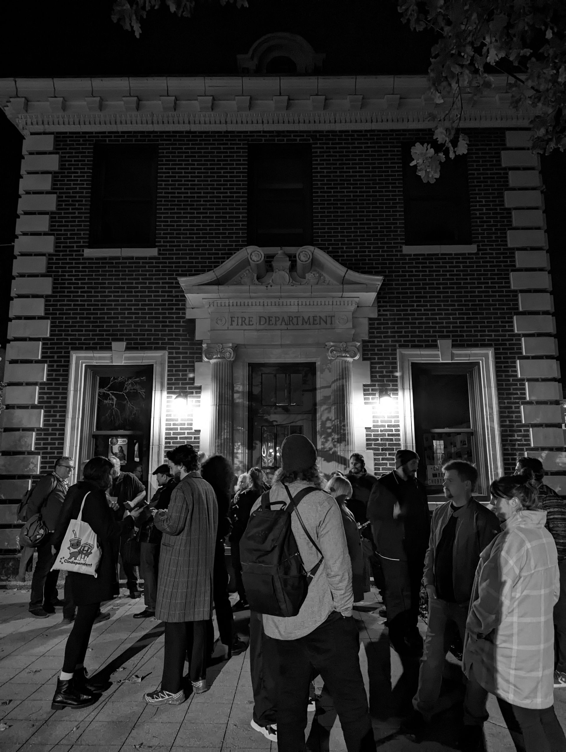 Group of people outside a brick building at night, lit by streetlights.