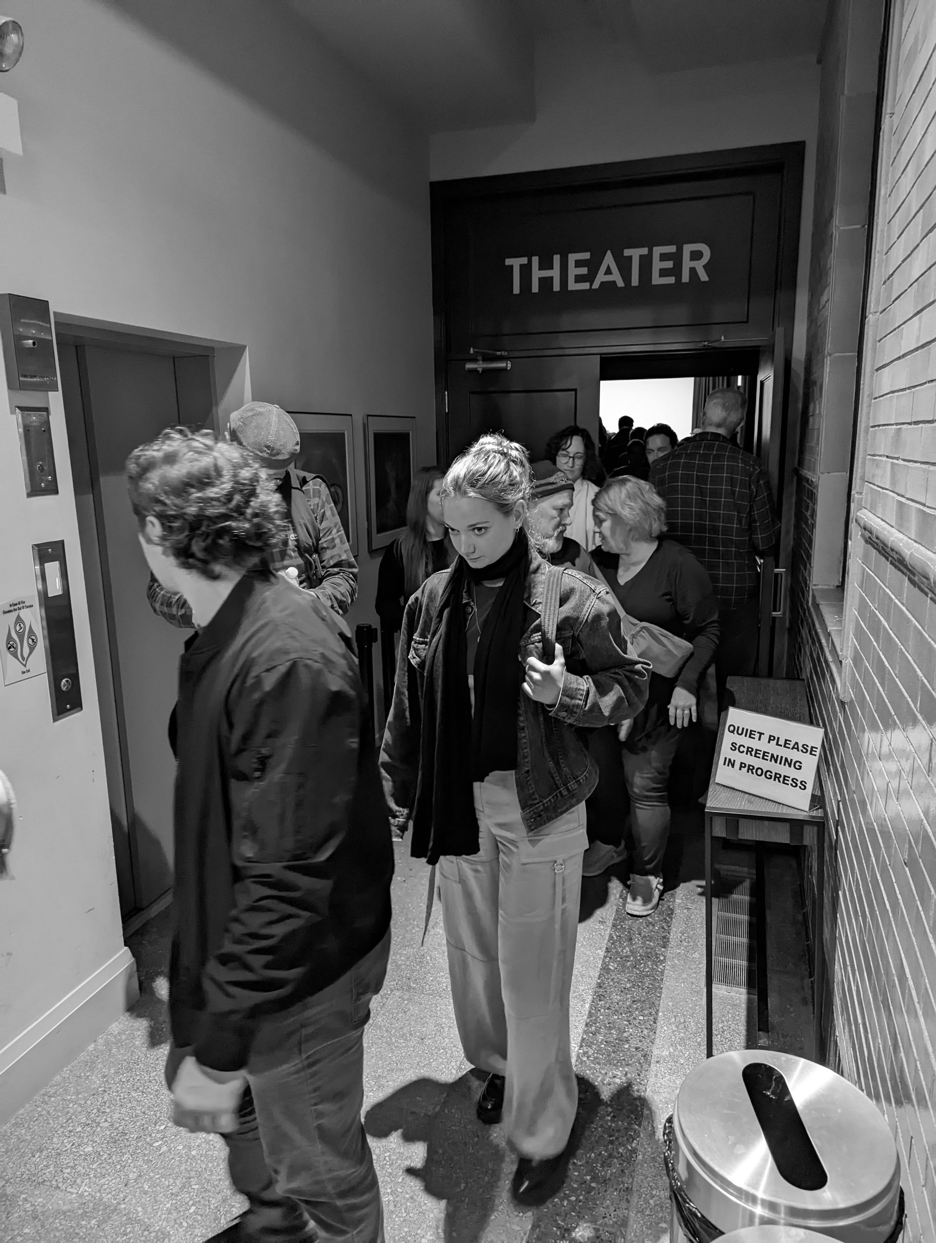 People entering a theater through a doorway. An elevator is to the left.