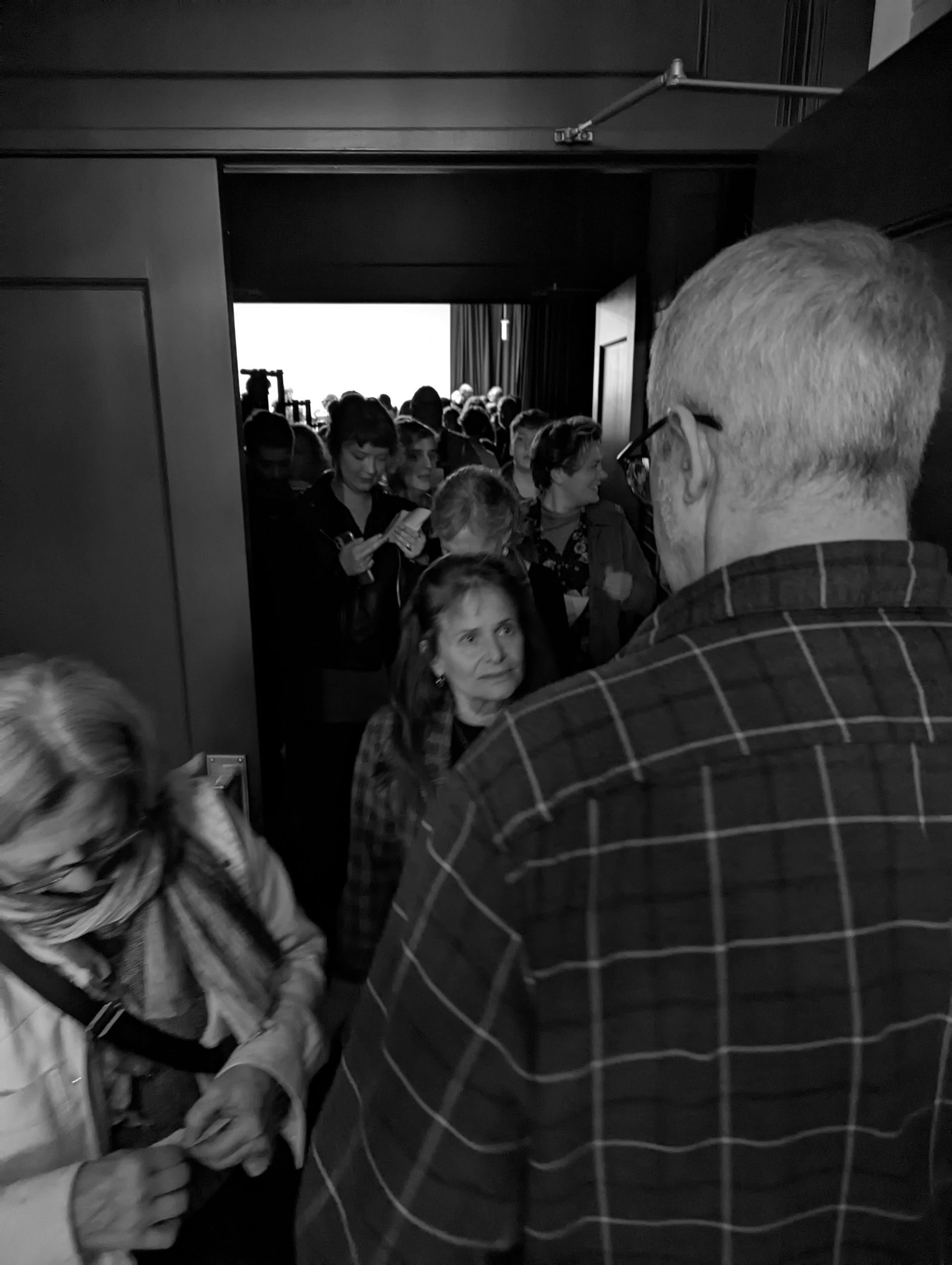People waiting in a doorway. A man in a plaid shirt faces the crowd. Others look forward expectantly.