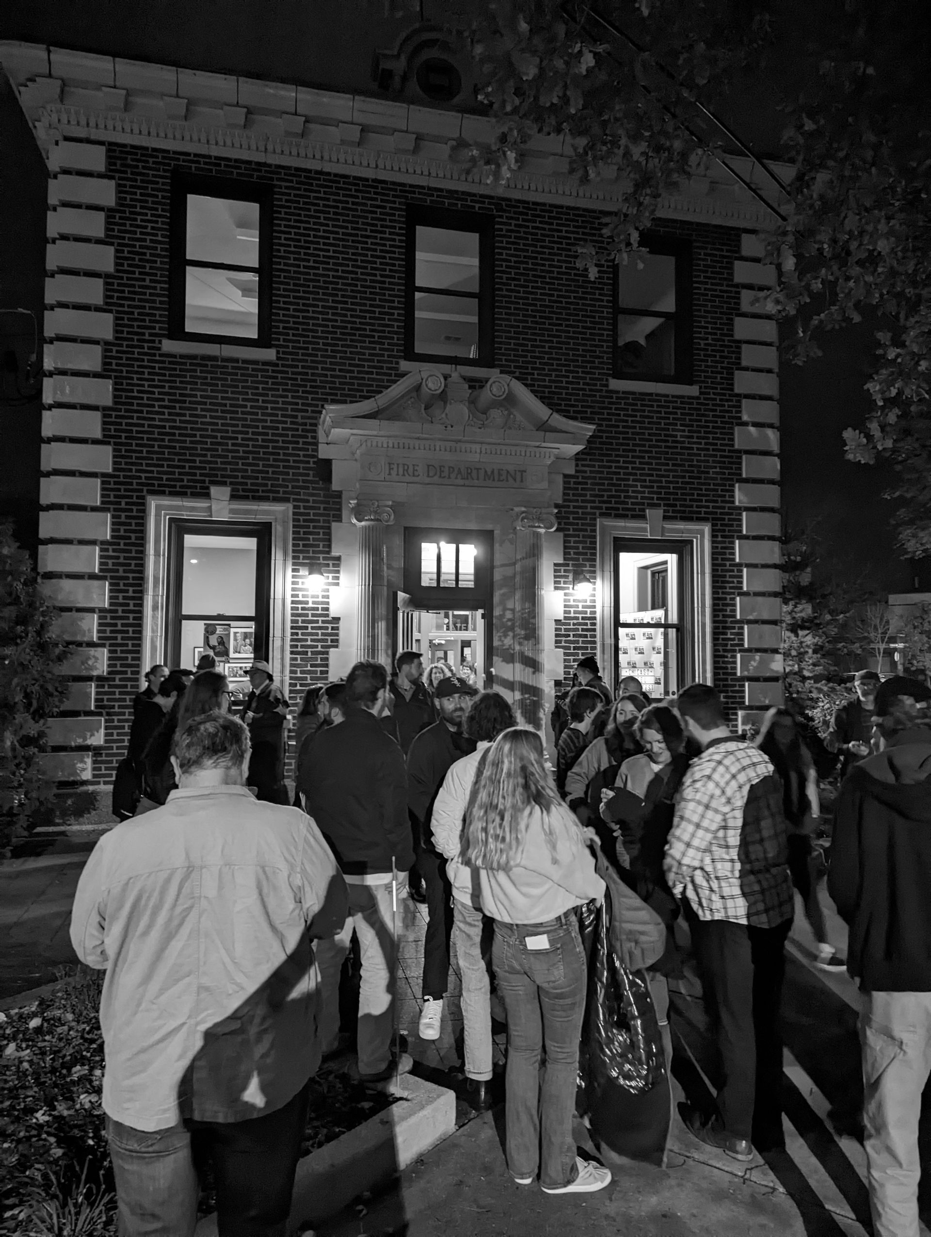 Black and white photo of a crowd in front of a brick building at night.