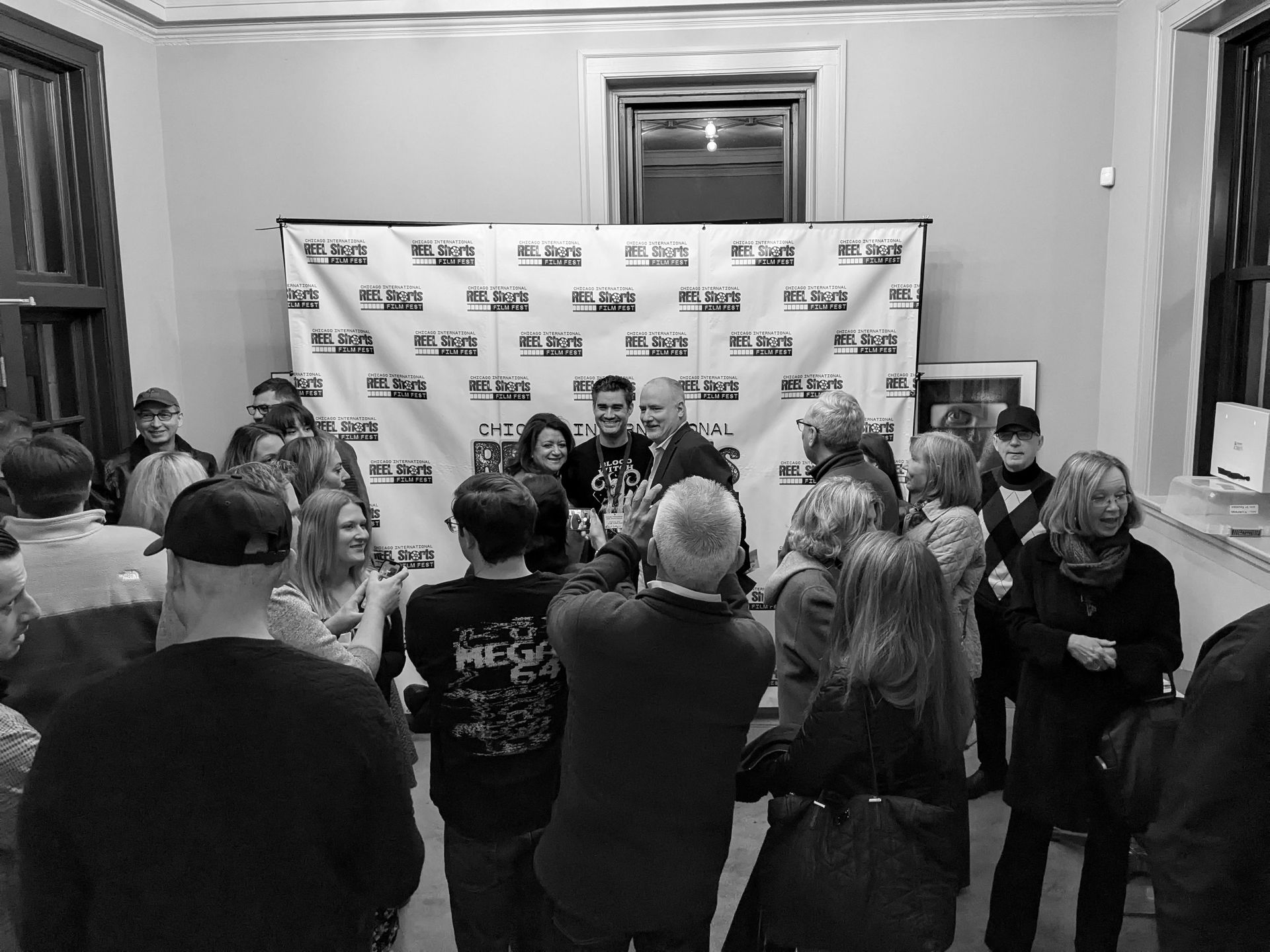 Group of people at an event with a backdrop featuring logos. People are taking photos.