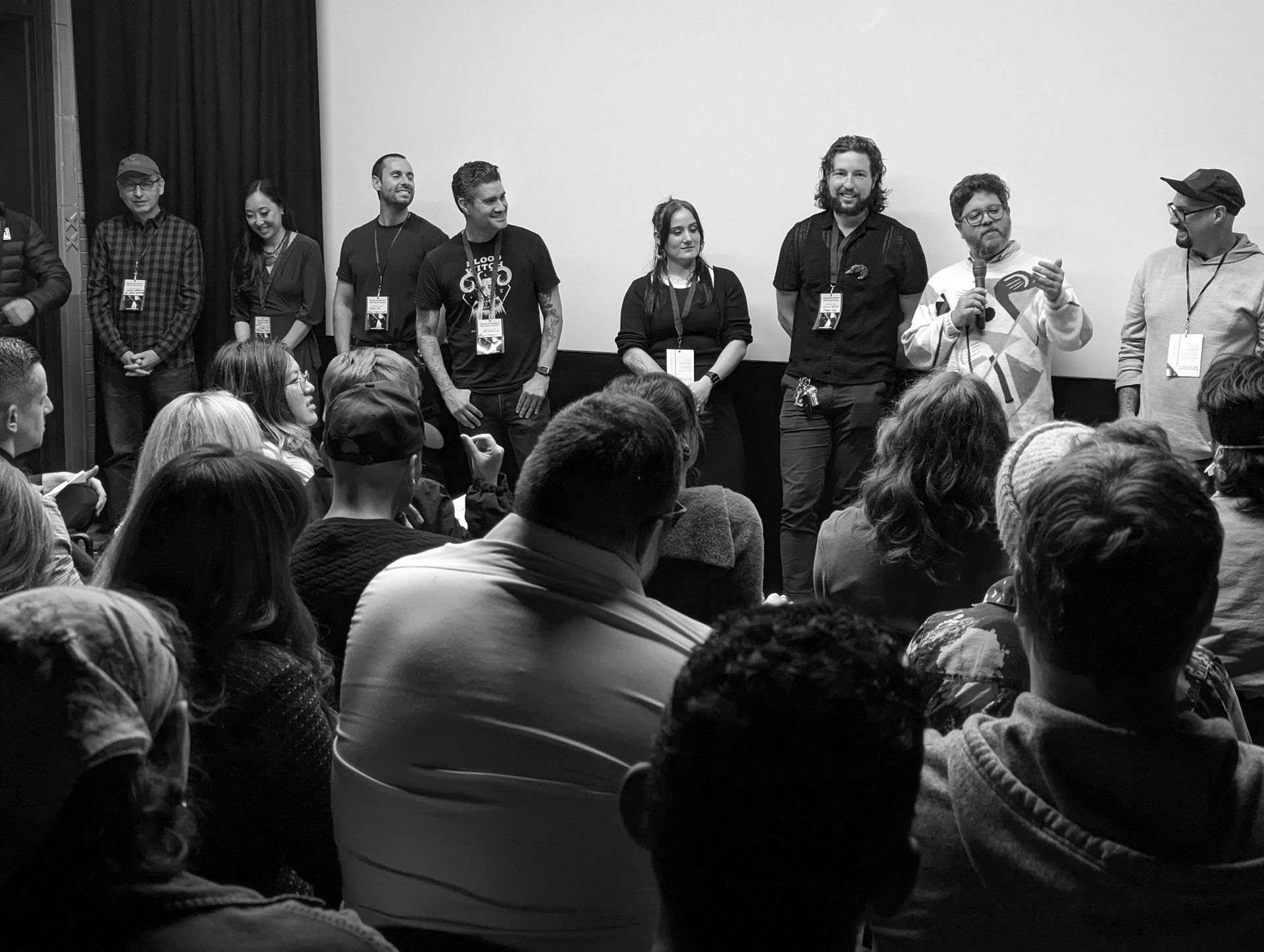 Group of people standing on a stage in front of an audience. Black and white photo.