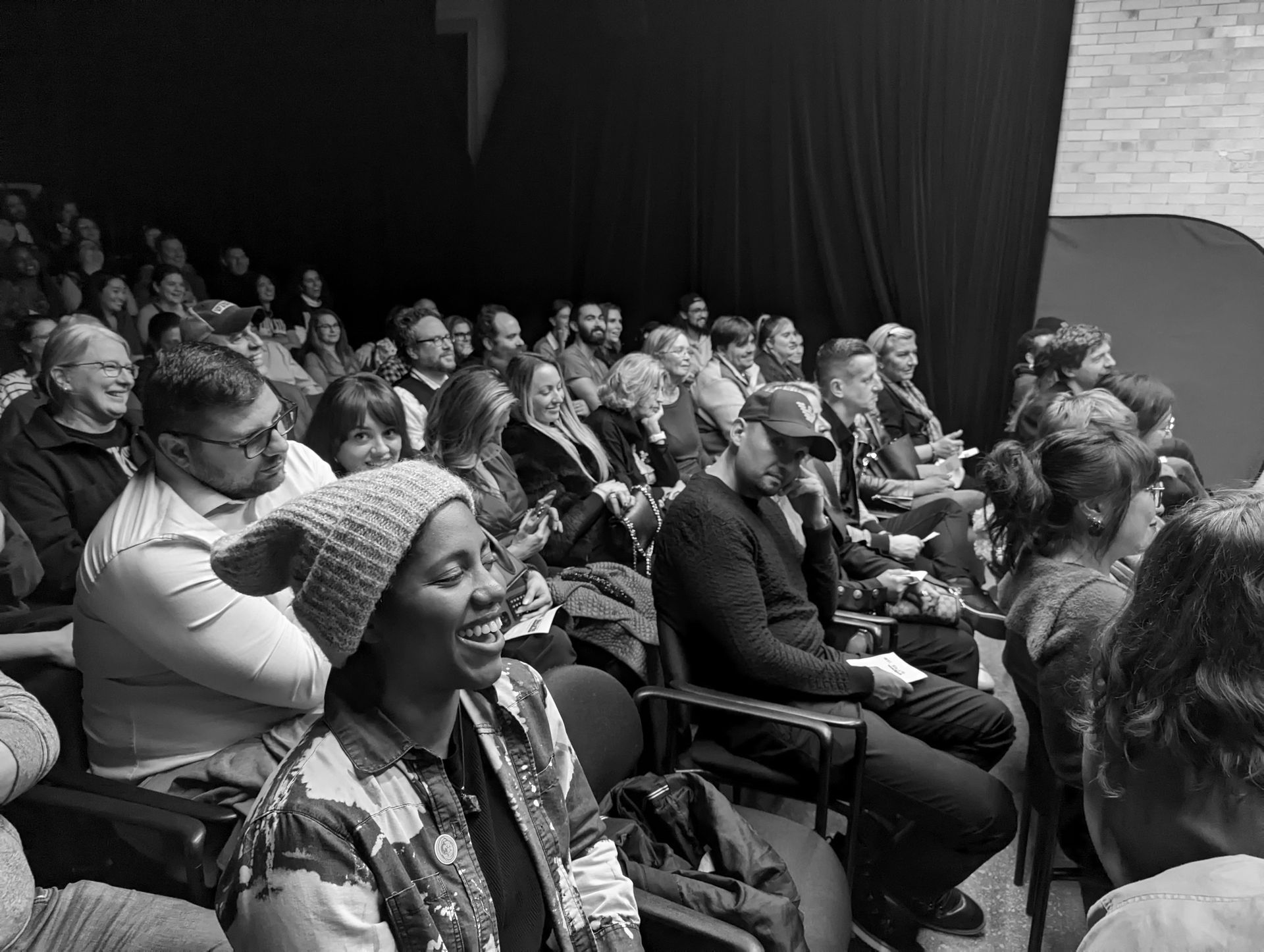 Audience in theater laughs, enjoying a performance. Black and white photo.