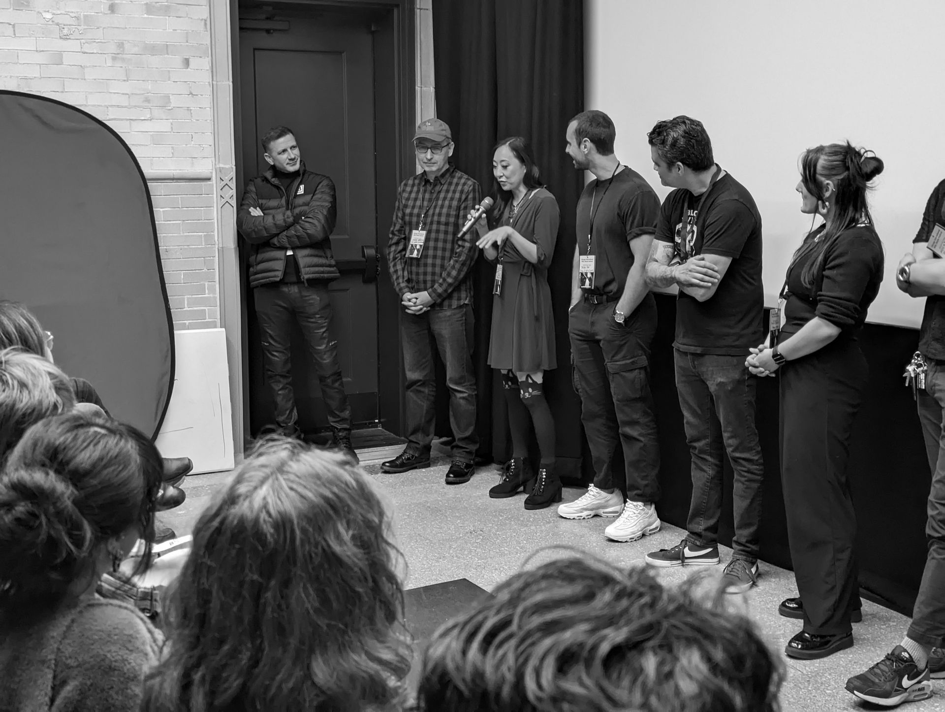 A group of people on stage, one speaking into a microphone. Black and white photo.